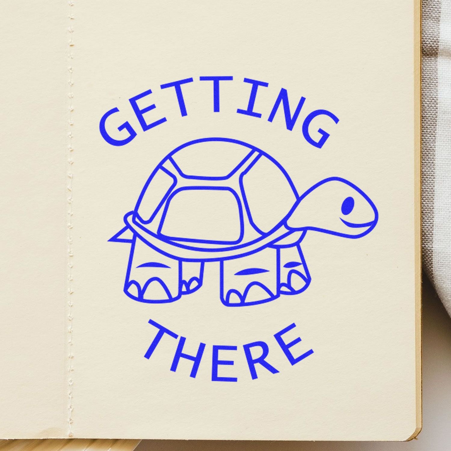 Round Getting There rubber stamp with a blue turtle illustration and the words Getting There stamped on a beige notebook page.