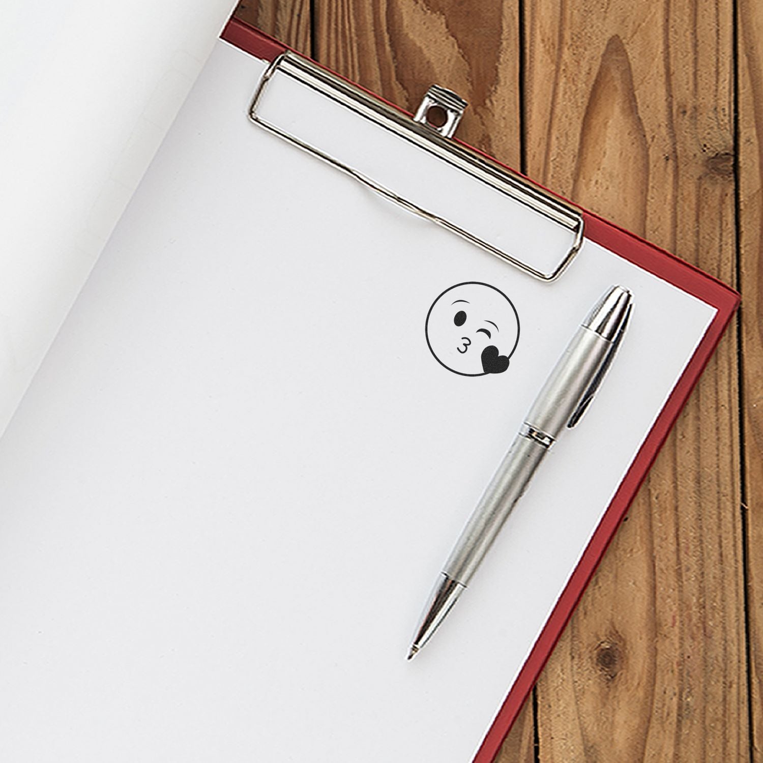 Round Happy Smiley Rubber Stamp on a white clipboard paper with a silver pen placed beside it on a wooden surface.