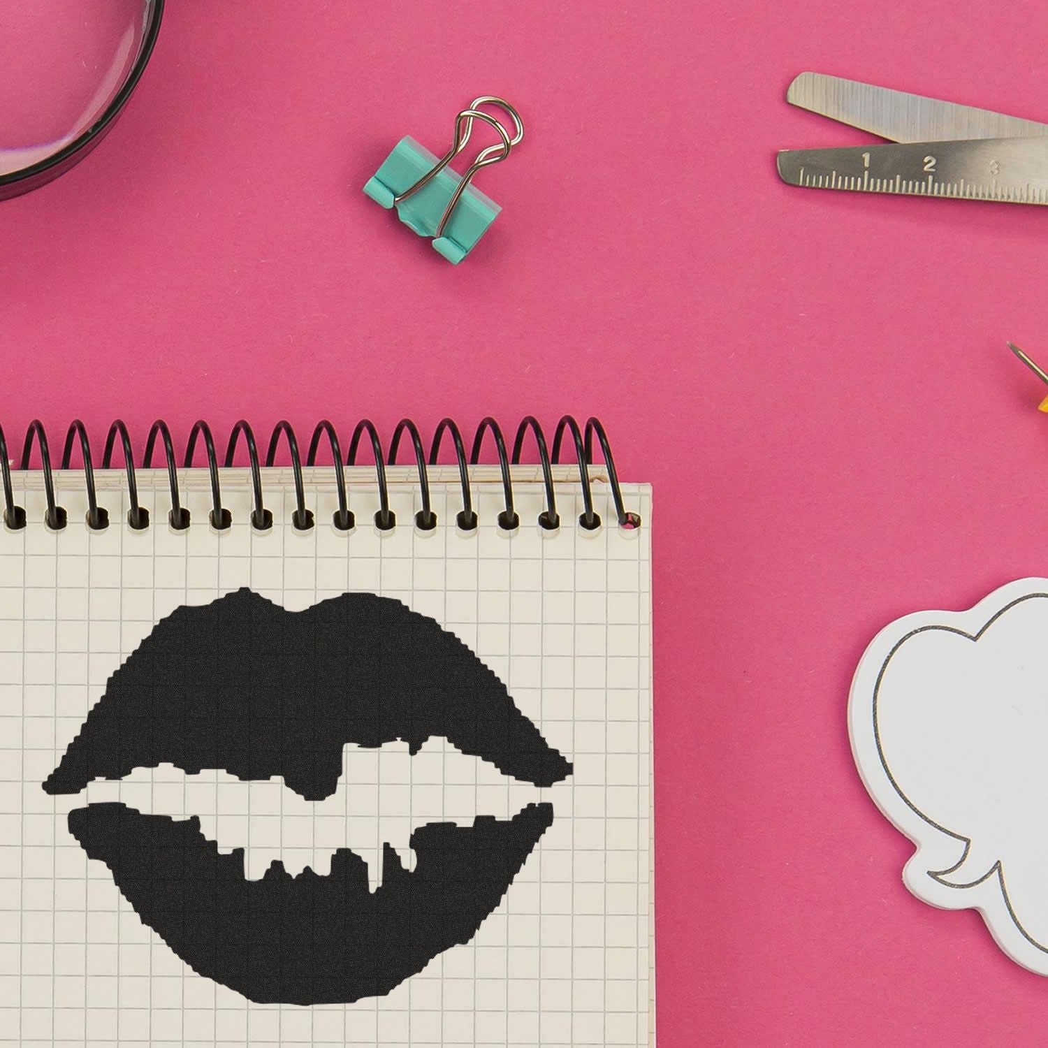 Round Kiss Rubber Stamp imprint on a spiral notebook, surrounded by stationery items on a pink background.