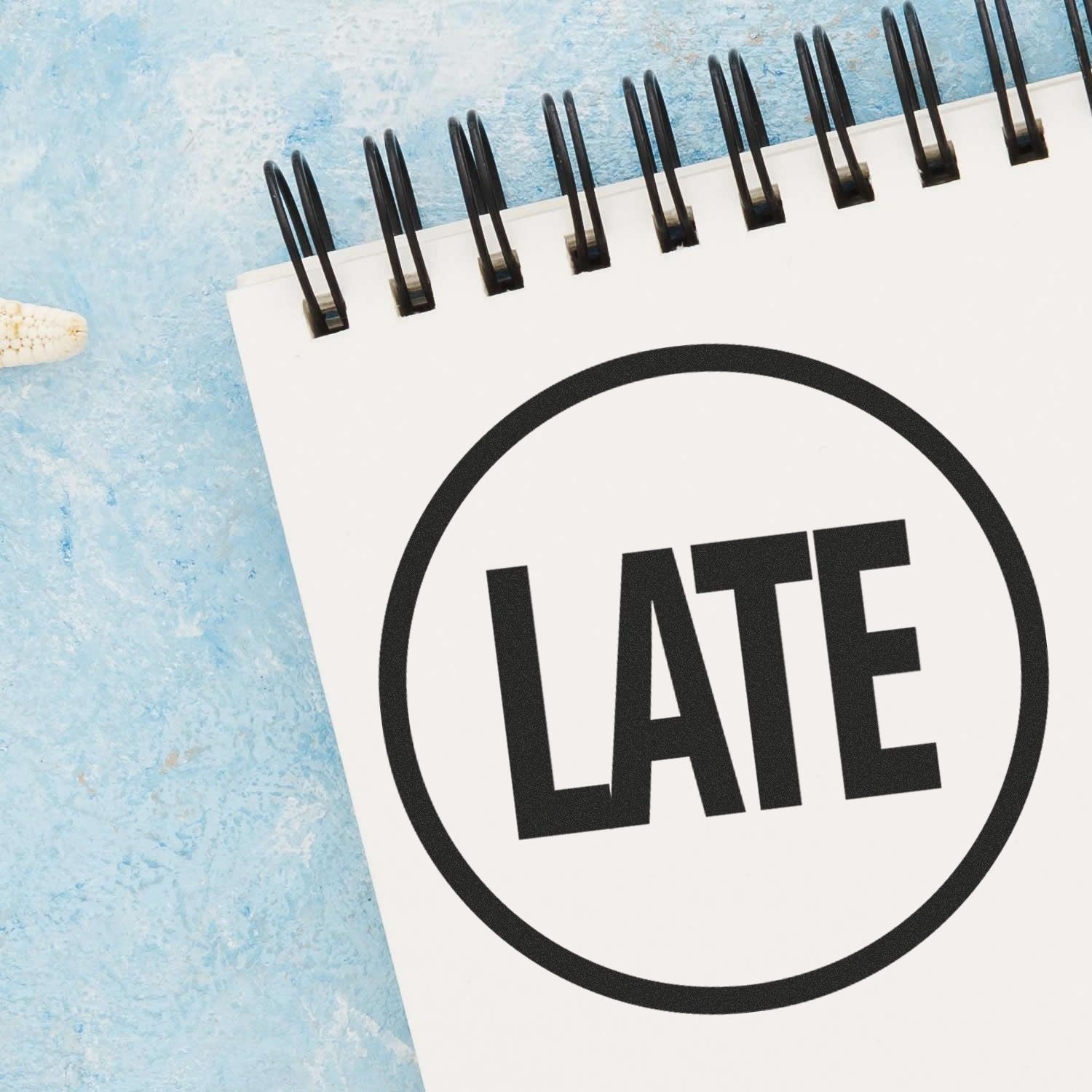 A Round Late Rubber Stamp imprint on a white notepad with a blue background. The stamp has the word "LATE" in bold letters inside a circle.