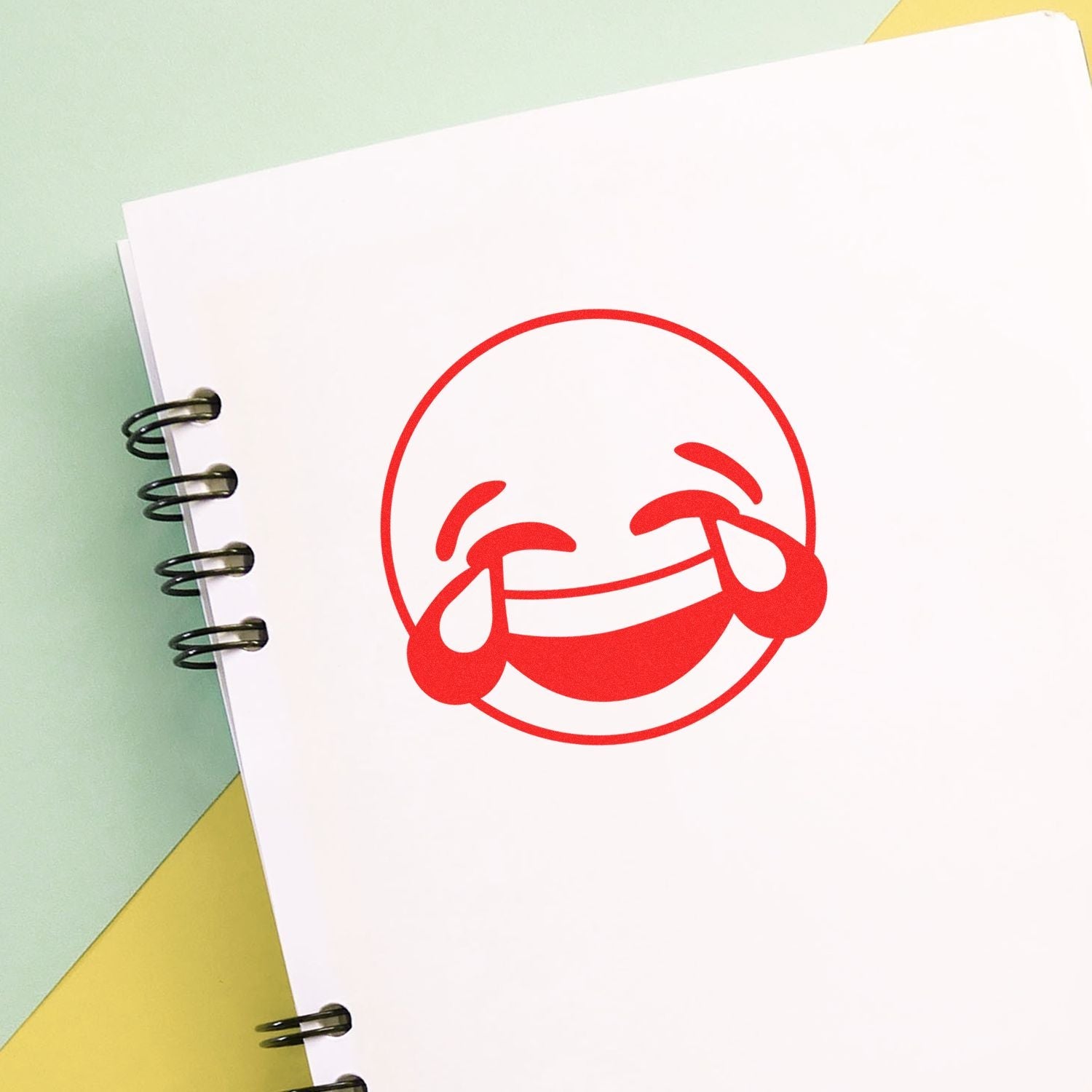 Self Inking Round Laughing Smiley Stamp imprint on white paper in a spiral notebook, showing a red laughing face with tears of joy.