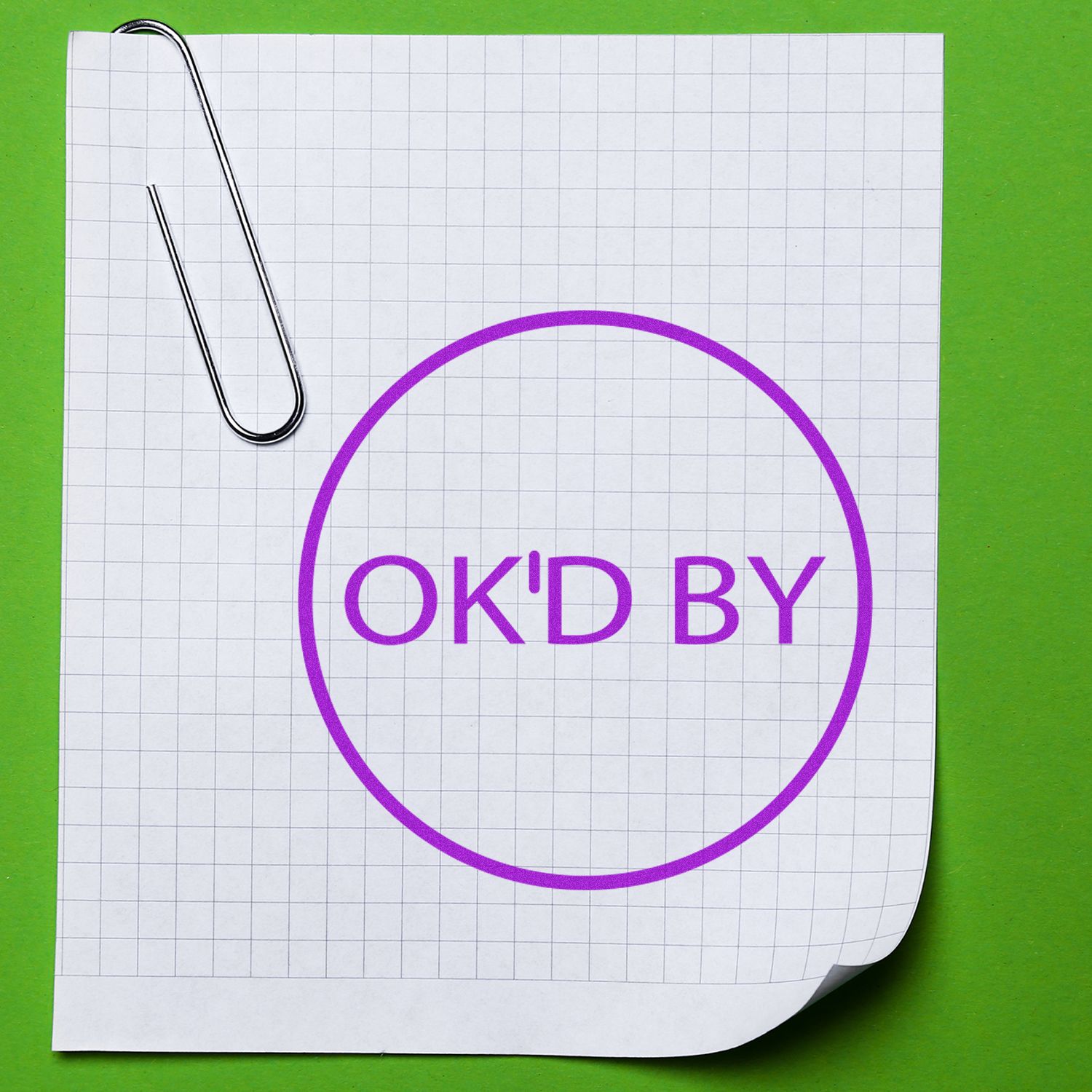 Self Inking Round Ok'd By Stamp in purple ink on a grid paper with a paperclip, placed on a green background.