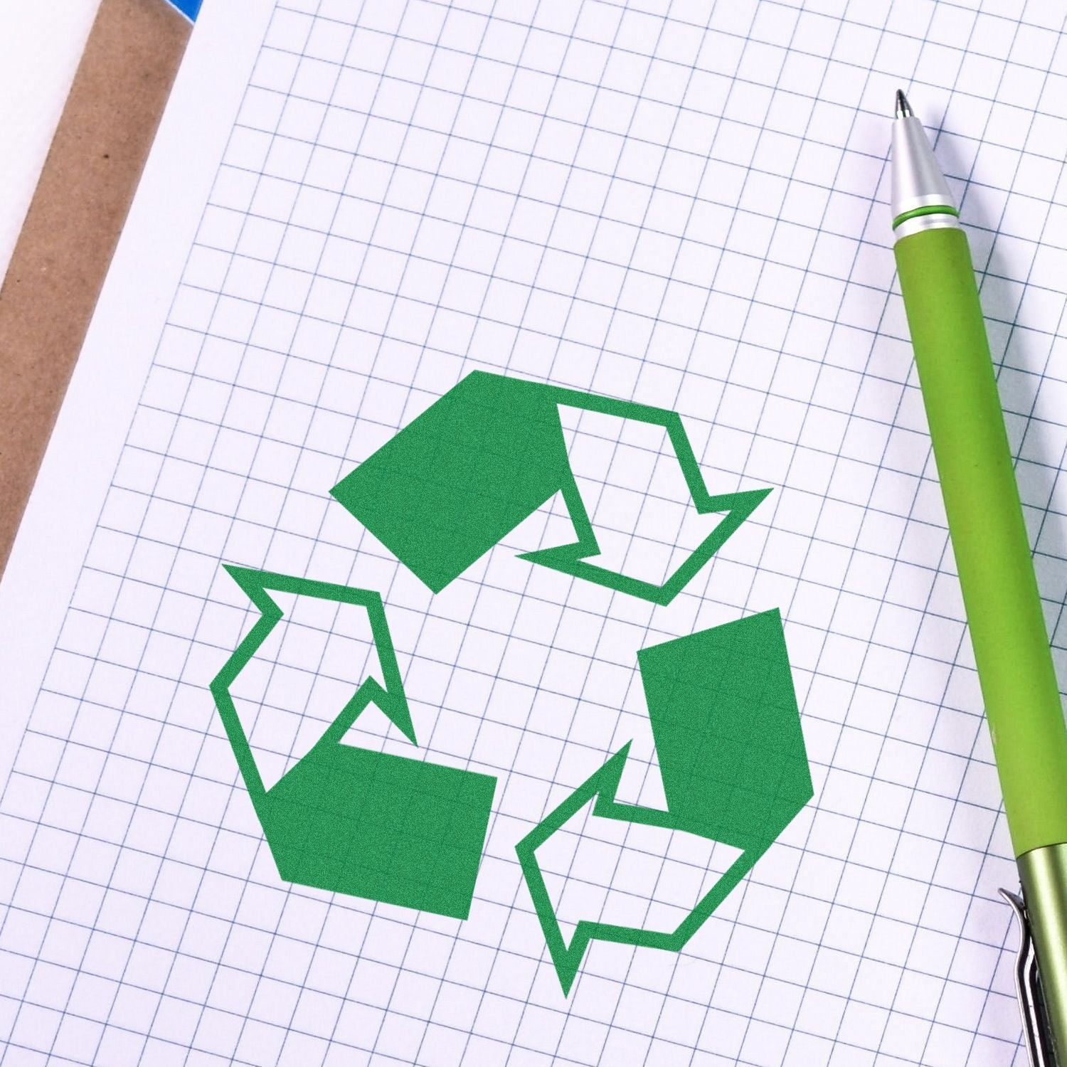 Self Inking Round Recycle Stamp imprint on graph paper with a green pen beside it. The stamp shows a green recycling symbol.