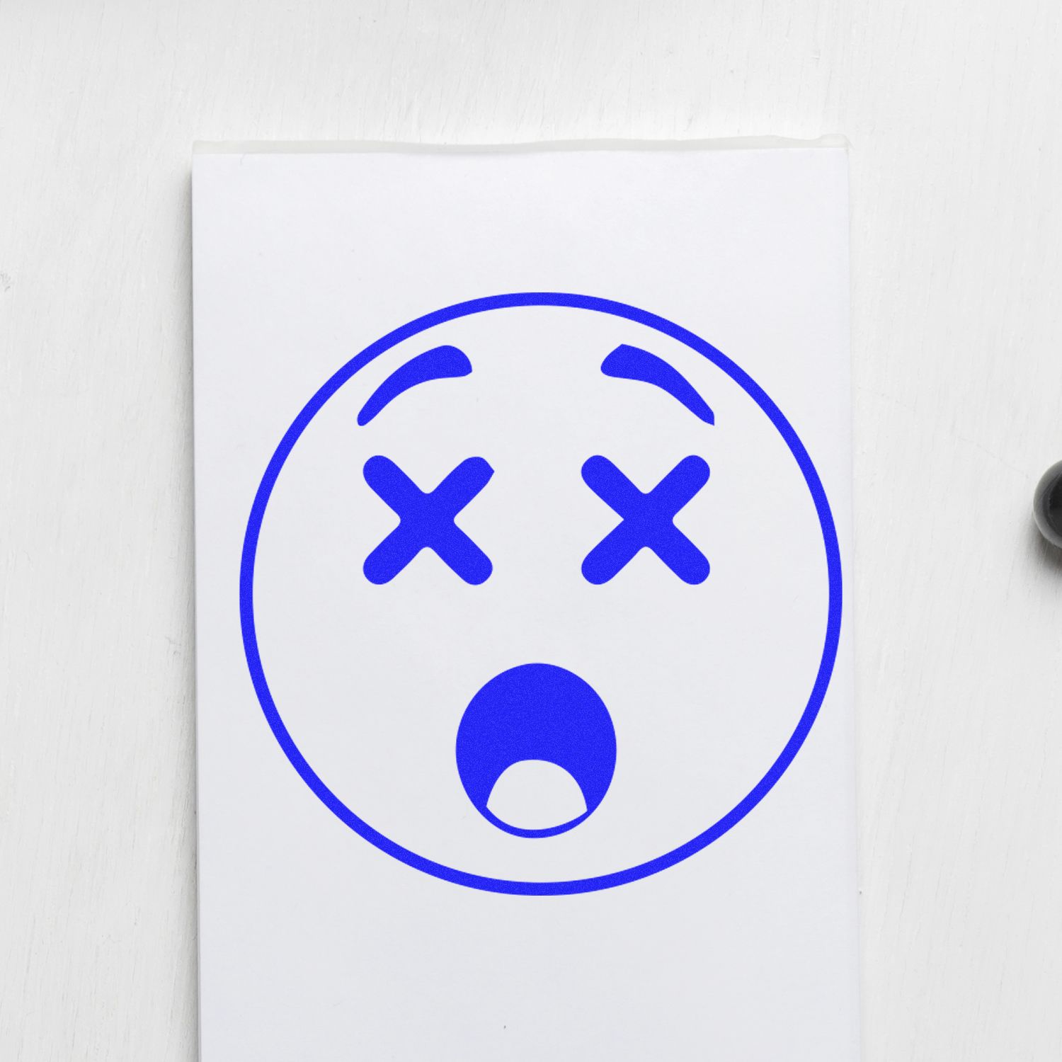 Round Shocked Smiley Rubber Stamp with X eyes and open mouth, stamped in blue ink on white paper.