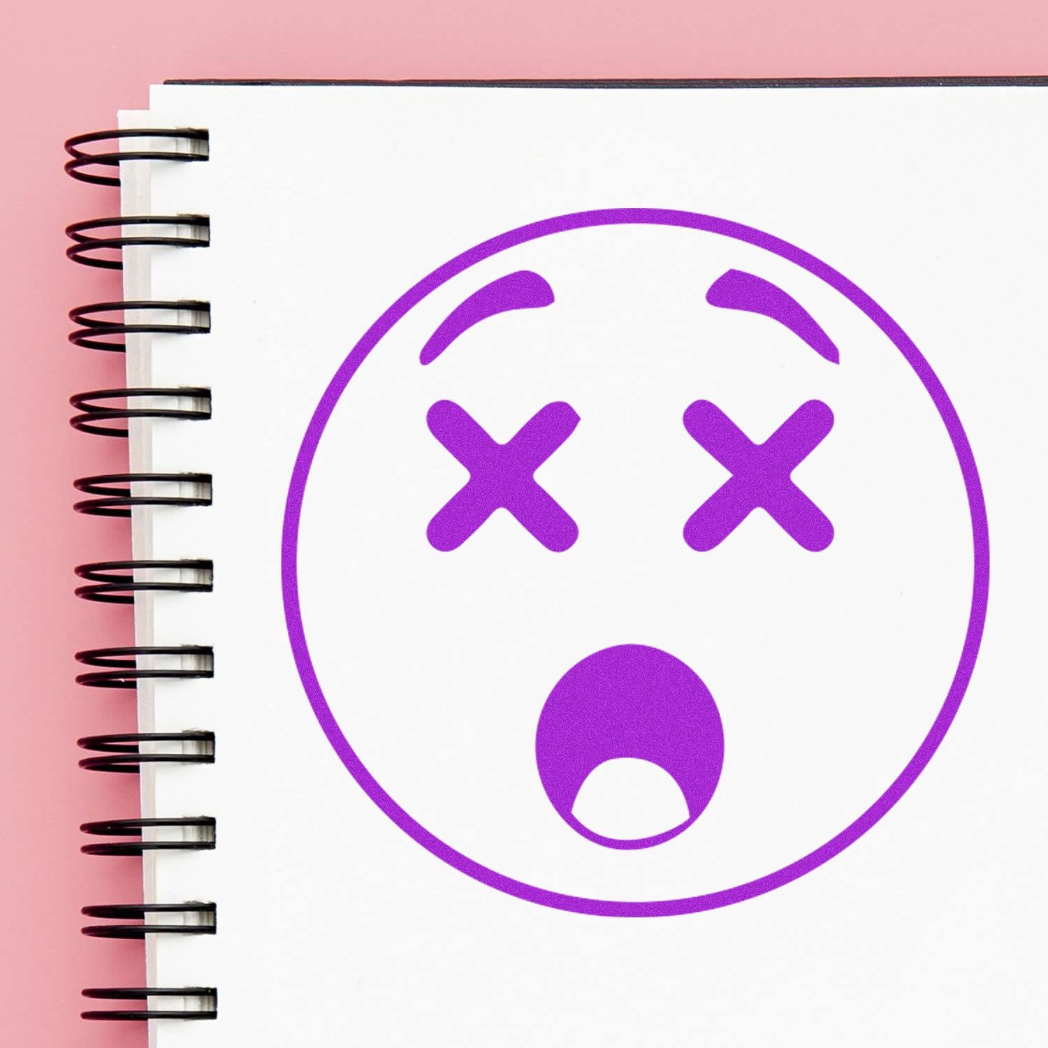 Round Shocked Smiley Rubber Stamp with a surprised expression on a spiral-bound notebook, featuring purple ink on white paper.