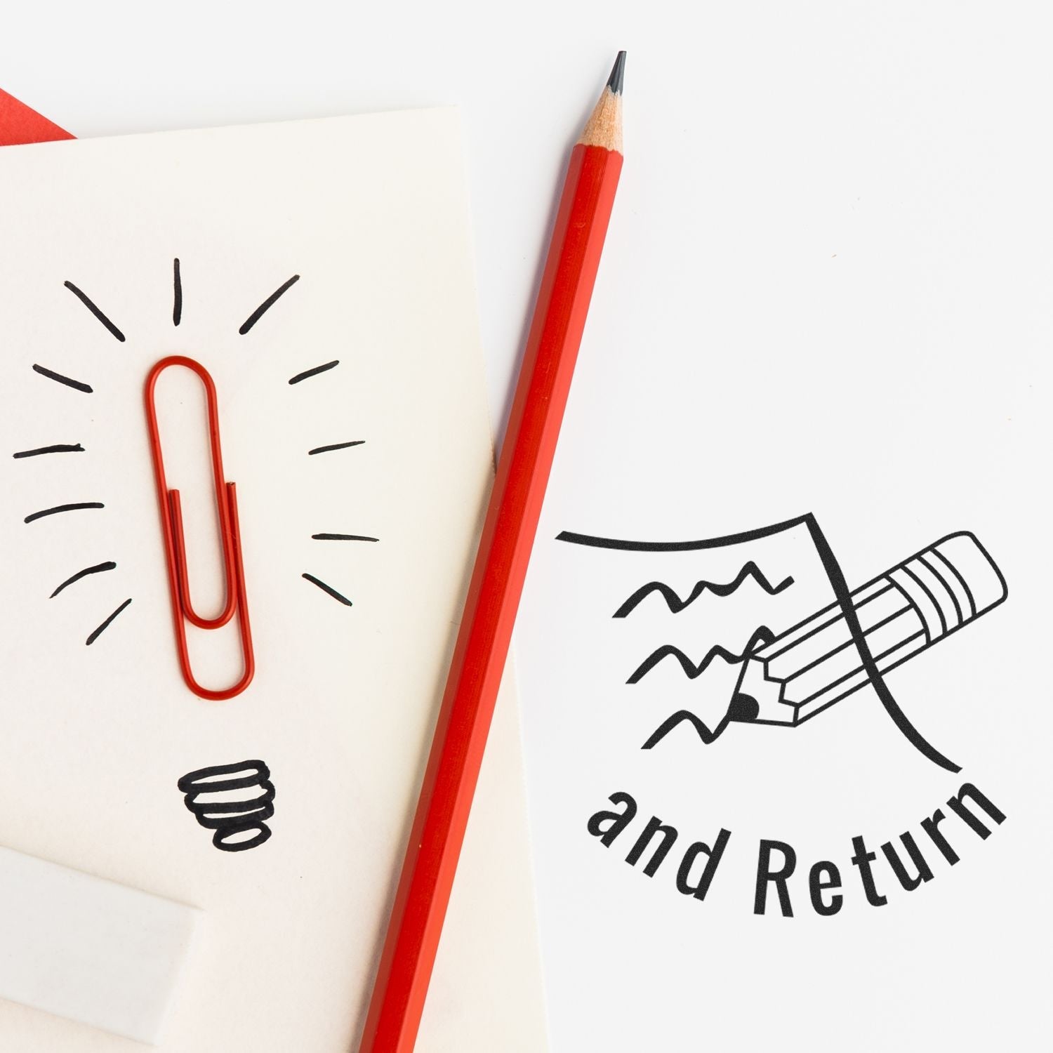 Self Inking Round Curious Smiley Stamp in use, featuring a red pencil and a paper clip on a white paper with and Return stamped.