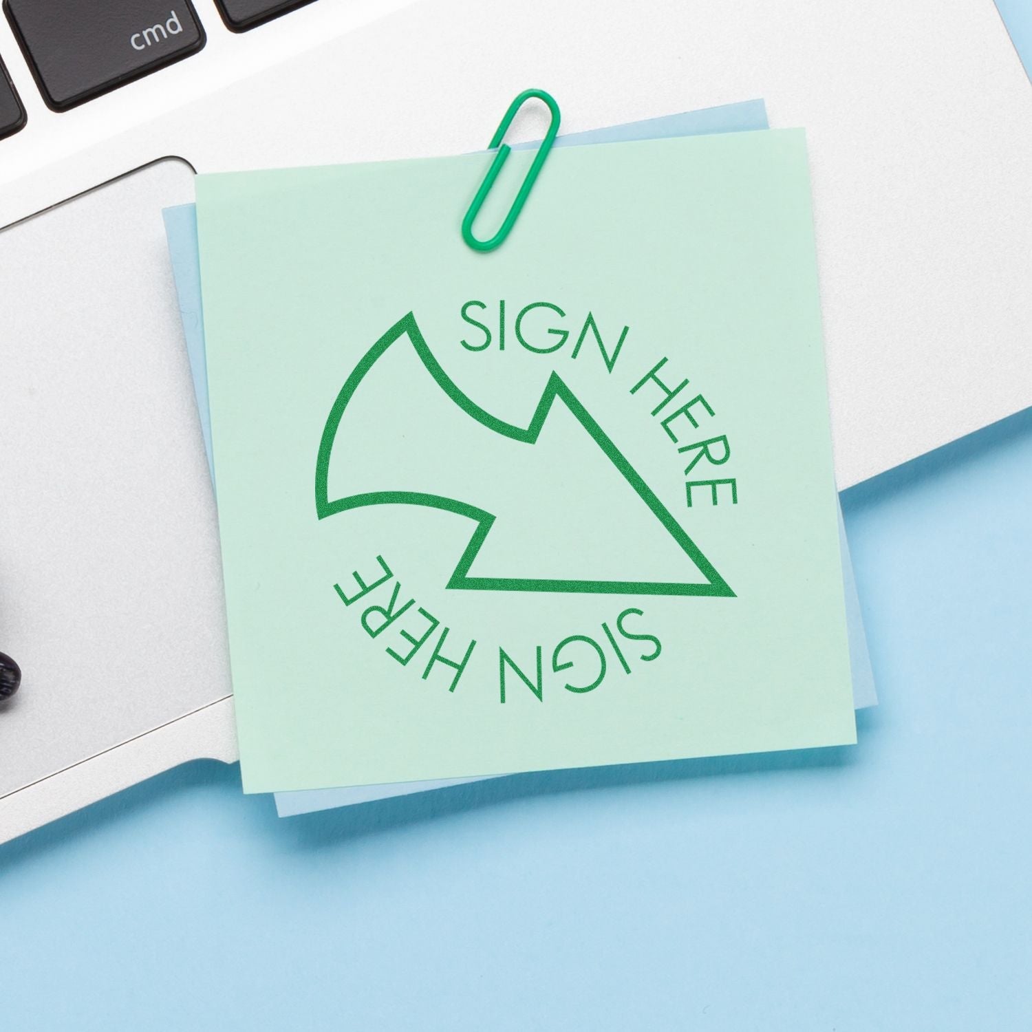 Self Inking Round Sign Here with Arrow Stamp on a green sticky note clipped to a laptop, indicating where to sign.