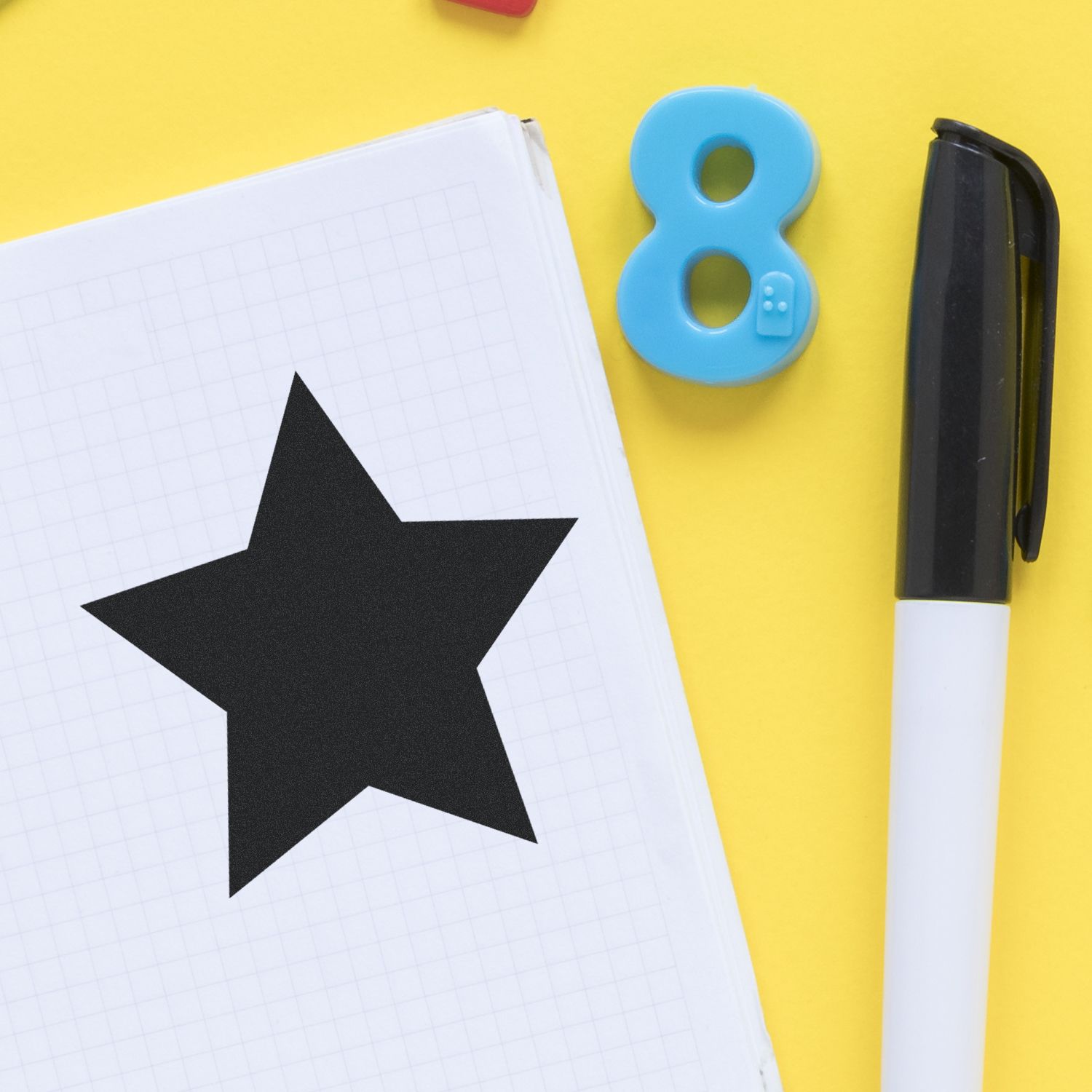 Round Solid Star Rubber Stamp impression on graph paper, with a black pen and blue number eight eraser on a yellow background.