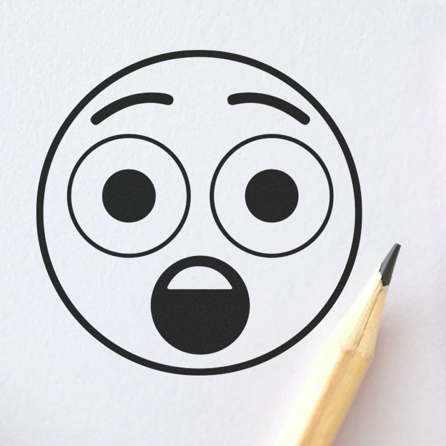 Self Inking Round Surprised Smiley Stamp impression on white paper with a pencil tip nearby.