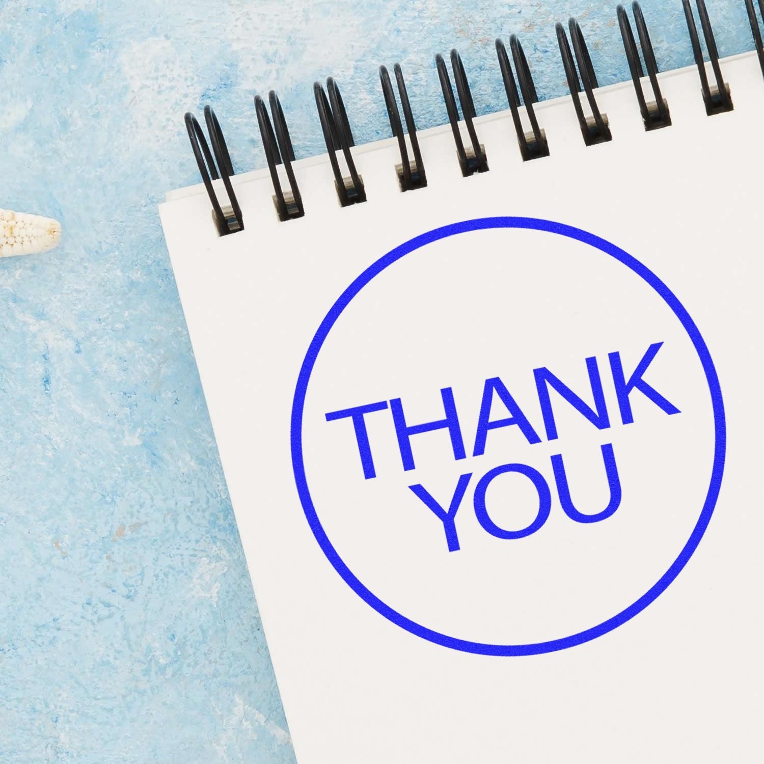 Self Inking Round Thank You Stamp imprint on a white notepad with a blue background.