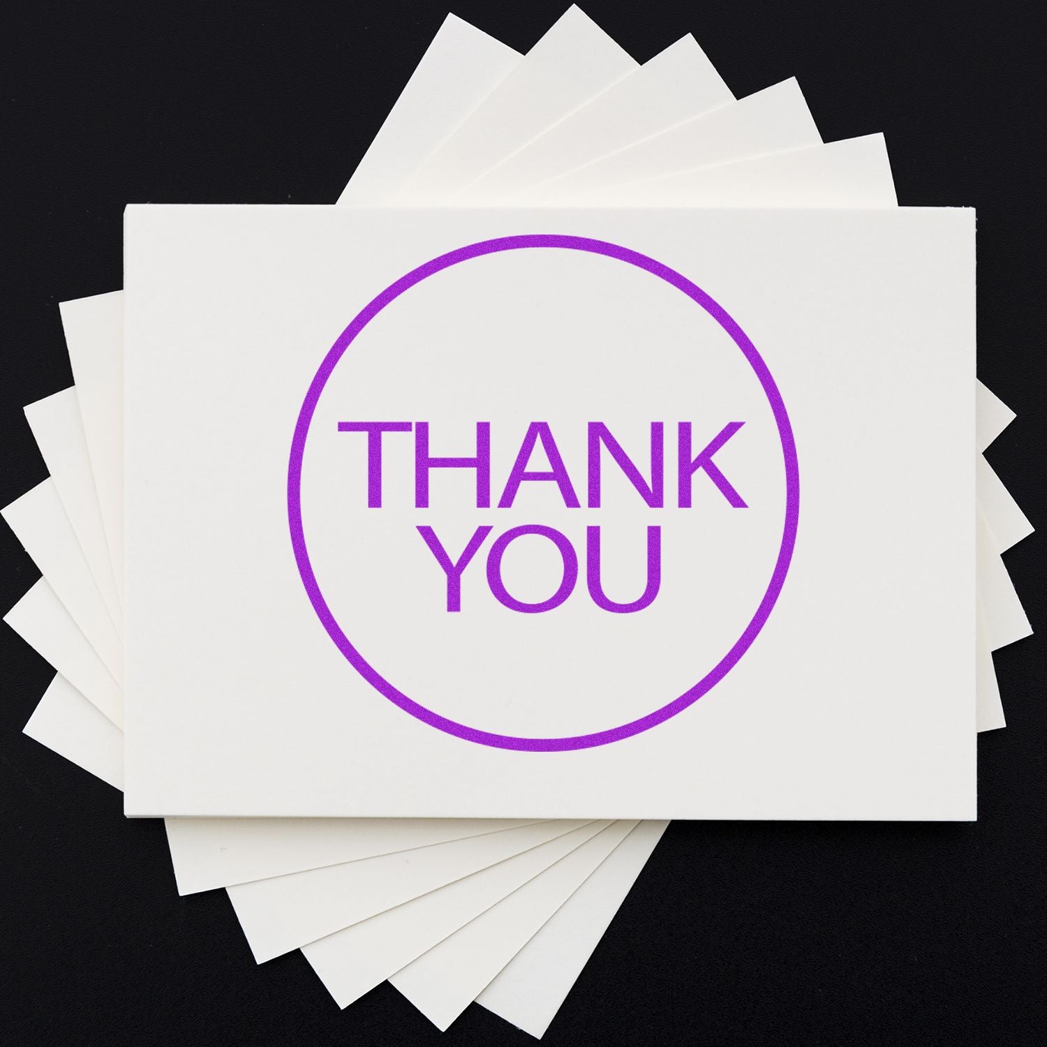 Round Thank You rubber stamp in purple ink on white cards, fanned out on a black background.