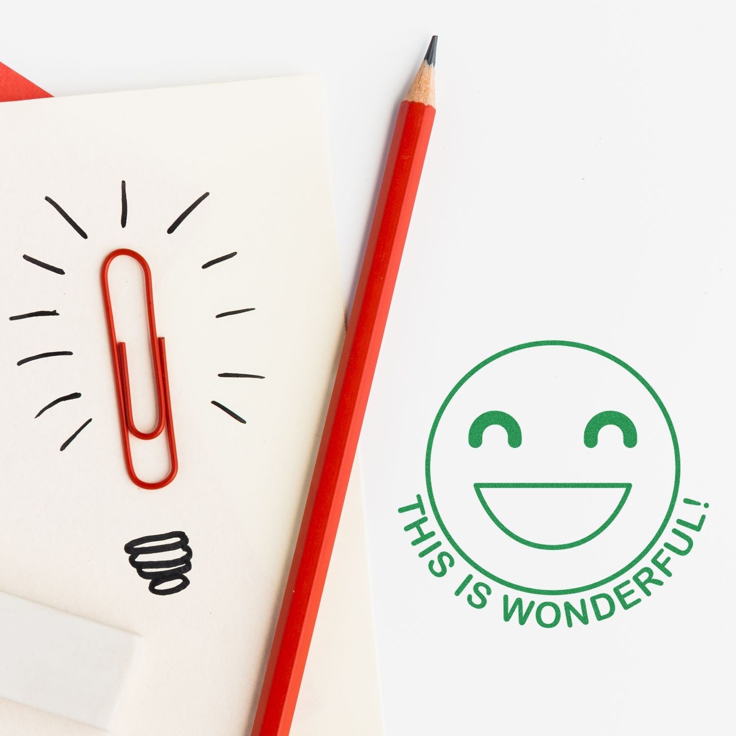 A red pencil and paperclip on a paper with a stamped green smiley face and text THIS IS WONDERFUL! using the Round This is Wonderful Smiley Self-Inking Stamp.