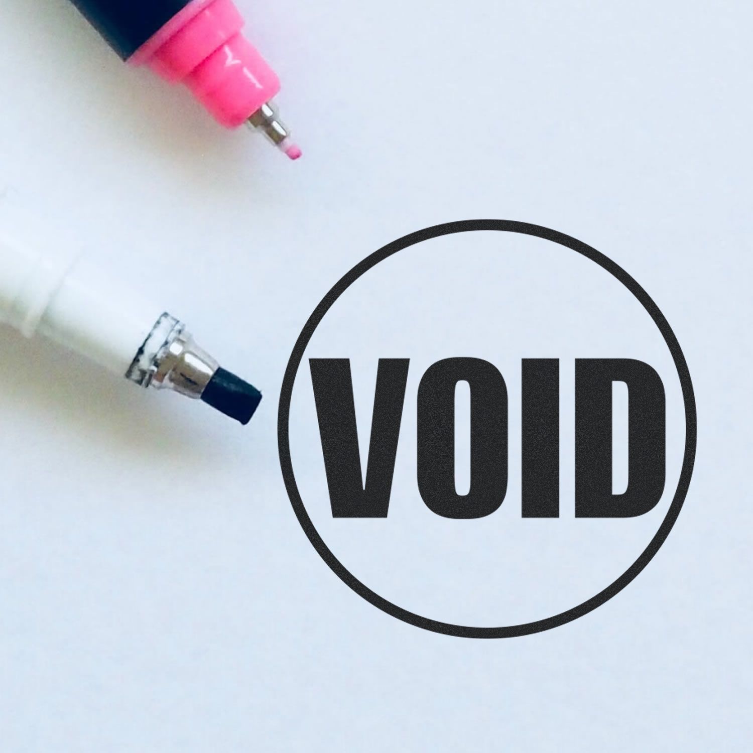 Round Void Rubber Stamp in black ink next to two markers, one pink and one white, on a white background.