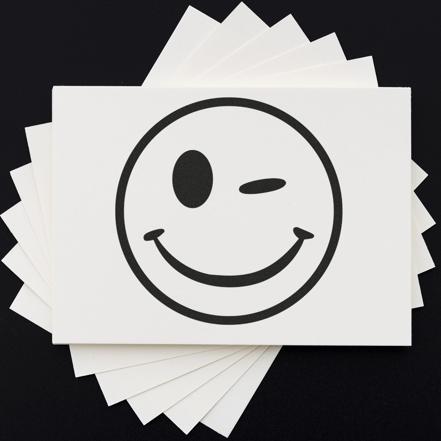 Round Winking Smiley Rubber Stamp on white paper with a black background, showing a playful winking face.