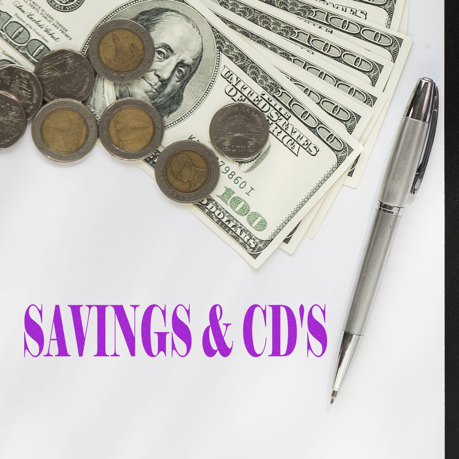 Large Savings & CD's Rubber Stamp next to a pen, coins, and dollar bills on a white surface with SAVINGS & CD'S text in purple.