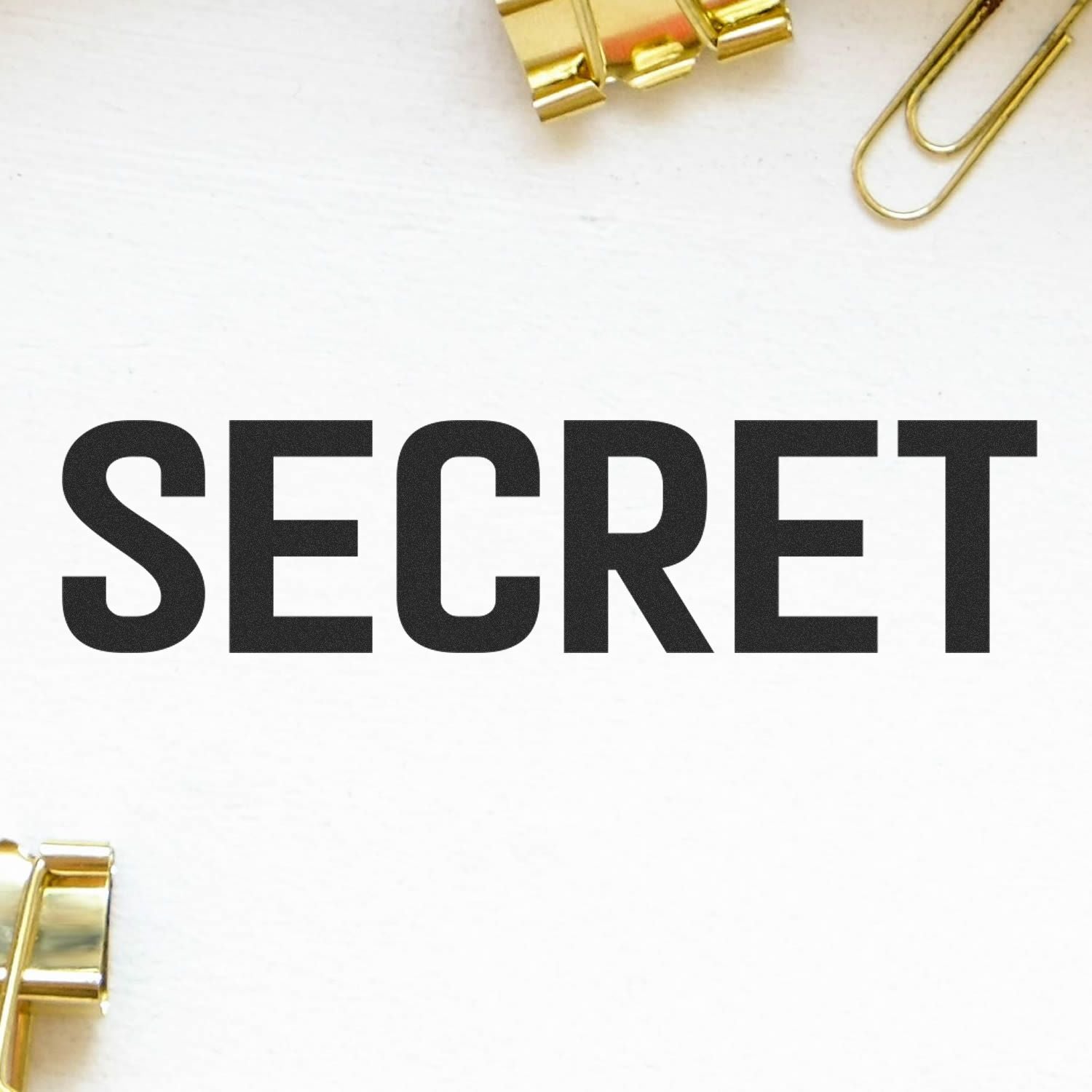 Large Self Inking Secret Stamp imprinting the word SECRET in bold black letters on a white surface, surrounded by gold office clips.