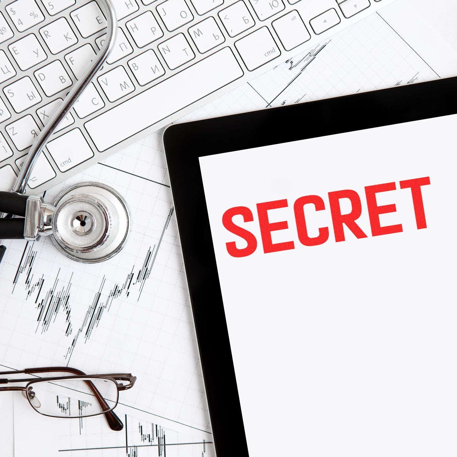 Tablet displaying the word SECRET in red, stamped using the Large Secret Rubber Stamp, placed on a desk with a keyboard, stethoscope, and glasses.