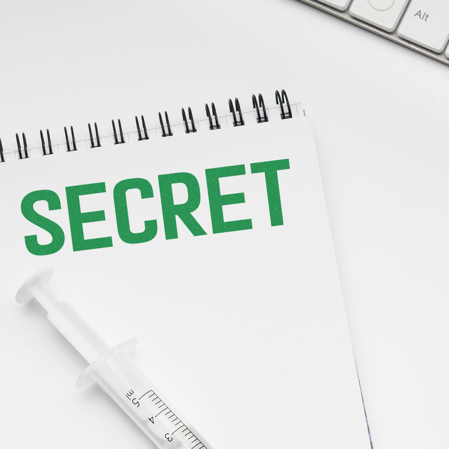 A notebook with SECRET stamped in green using a Secret Rubber Stamp, next to a syringe and a keyboard.