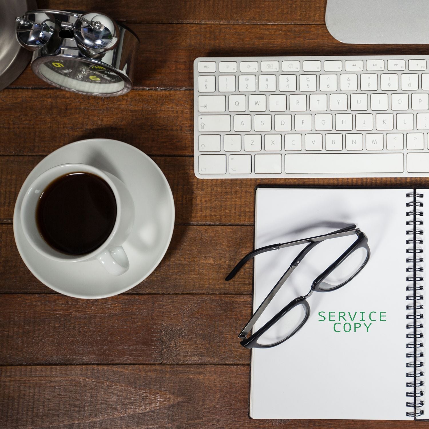 A desk with a keyboard, coffee cup, glasses, and a notebook stamped with SERVICE COPY using a large service copy rubber stamp.