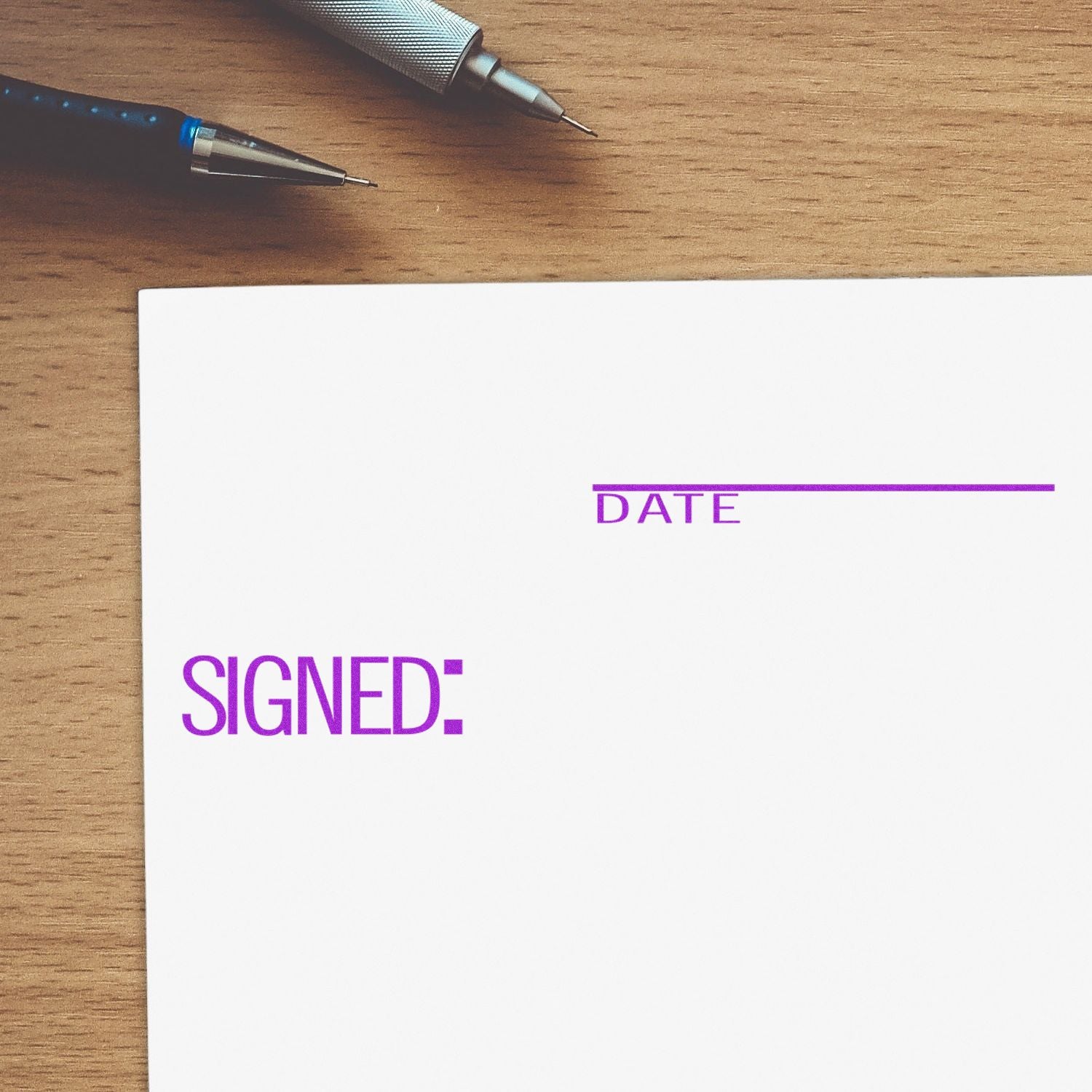 Large Signed with Date Rubber Stamp in purple ink on white paper, next to a pen on a wooden desk.