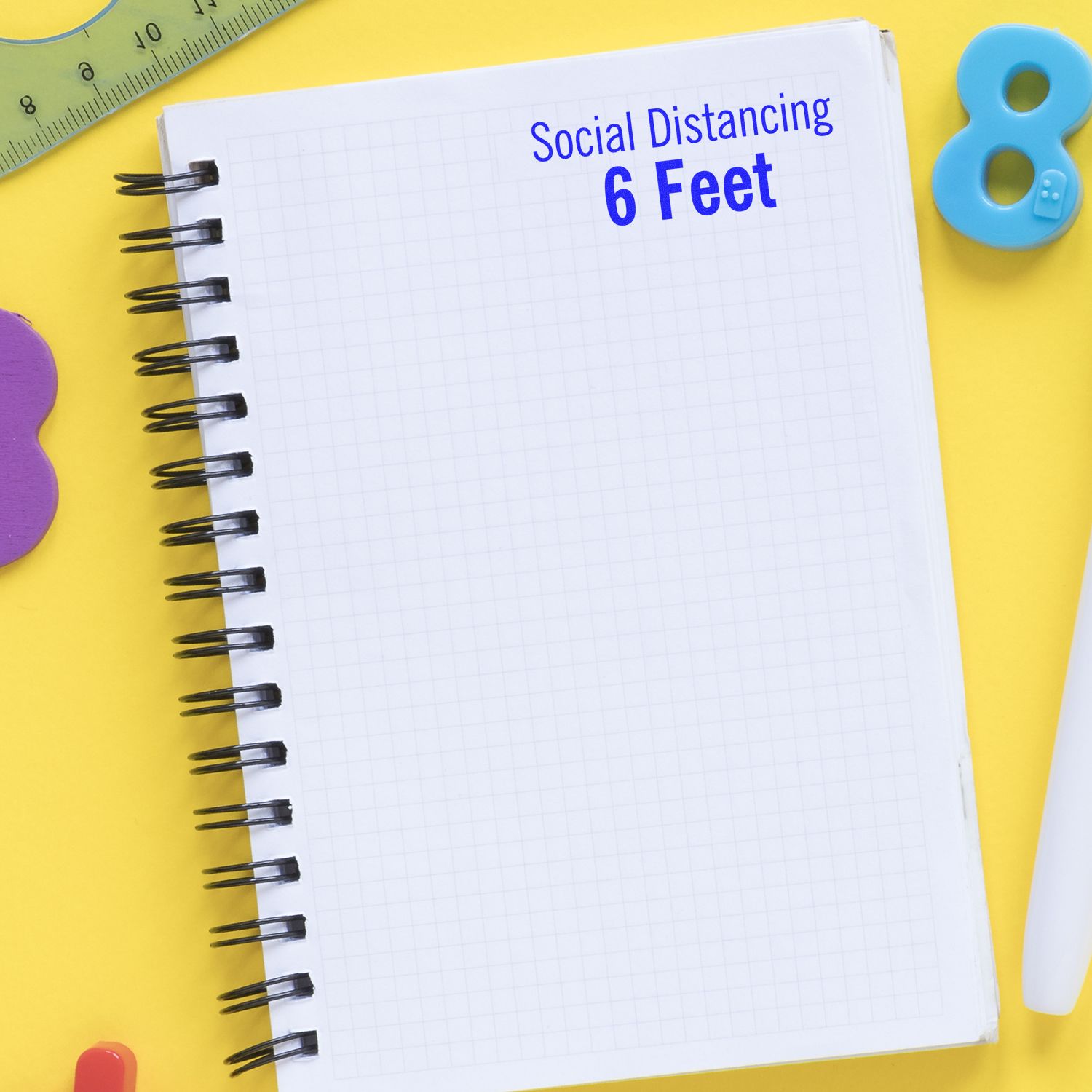 A notebook with a Social Distancing 6 Feet rubber stamp on a yellow background with various stationery items.