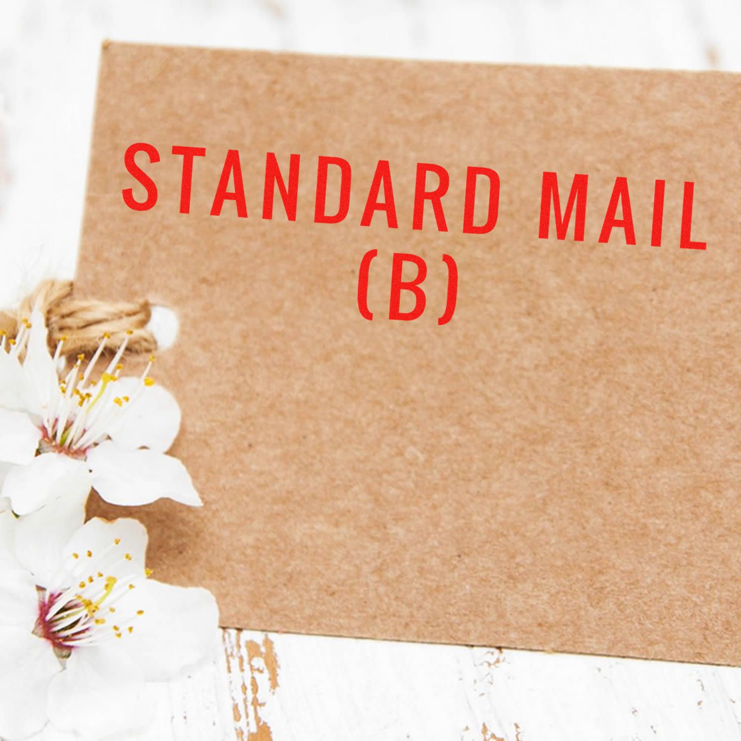 Brown card with STANDARD MAIL (B) in red text, adorned with white flowers on a rustic white wooden surface.