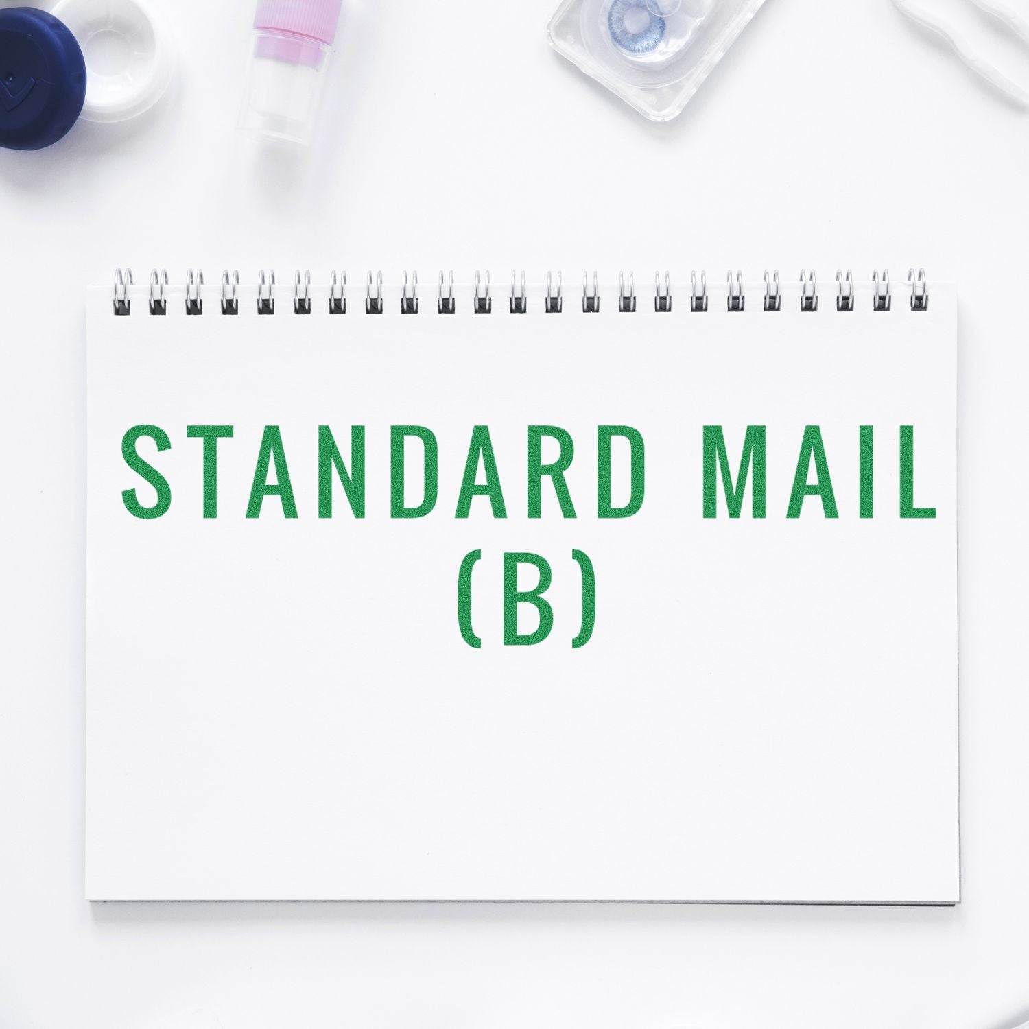 Large Pre-Inked Standard Mail (B) Stamp in green ink on a white spiral notebook, surrounded by office supplies.