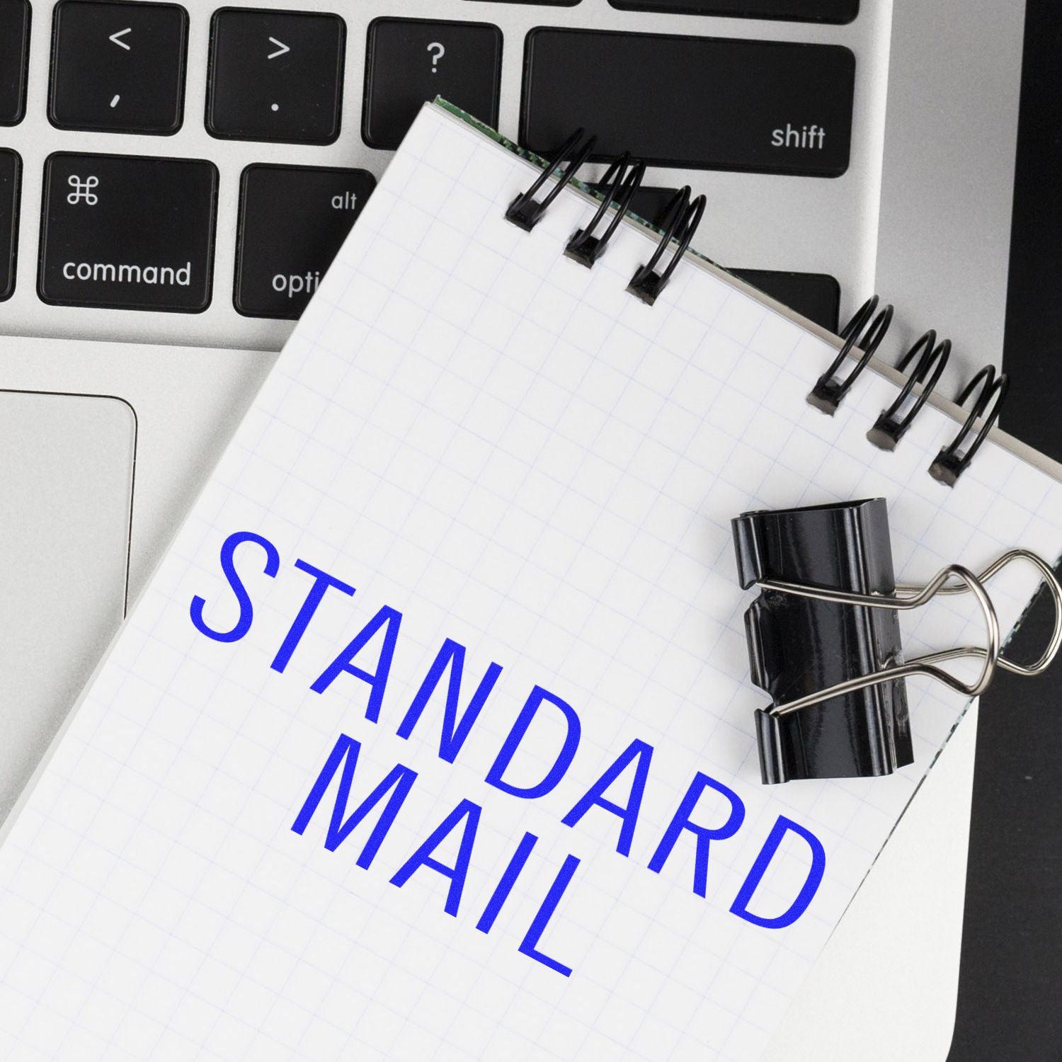 A notebook with STANDARD MAIL stamped in blue ink, placed on a laptop keyboard, next to a large standard mail stacked rubber stamp.