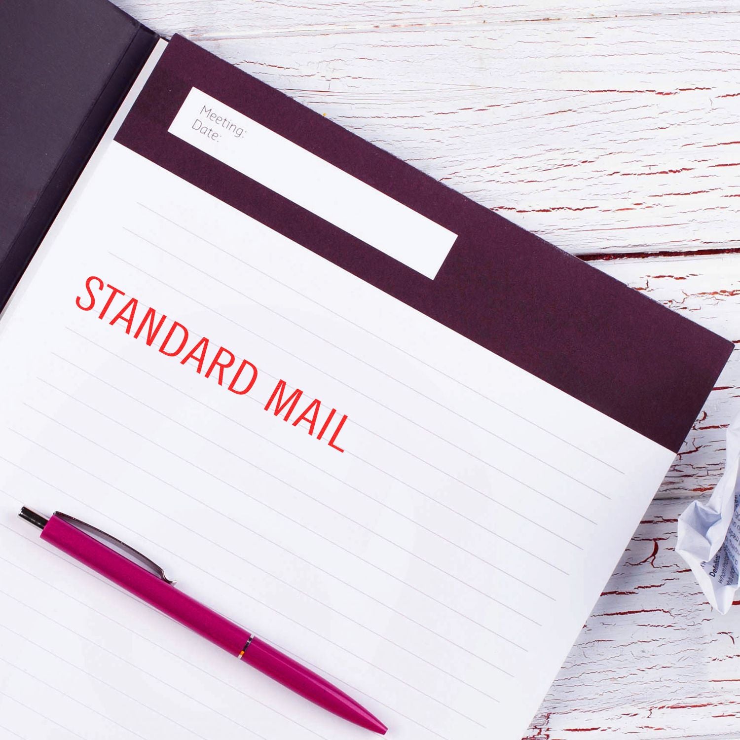 Self Inking Standard Mail Stamp imprint in red on a lined notebook page with a purple pen beside it, placed on a white wooden surface.