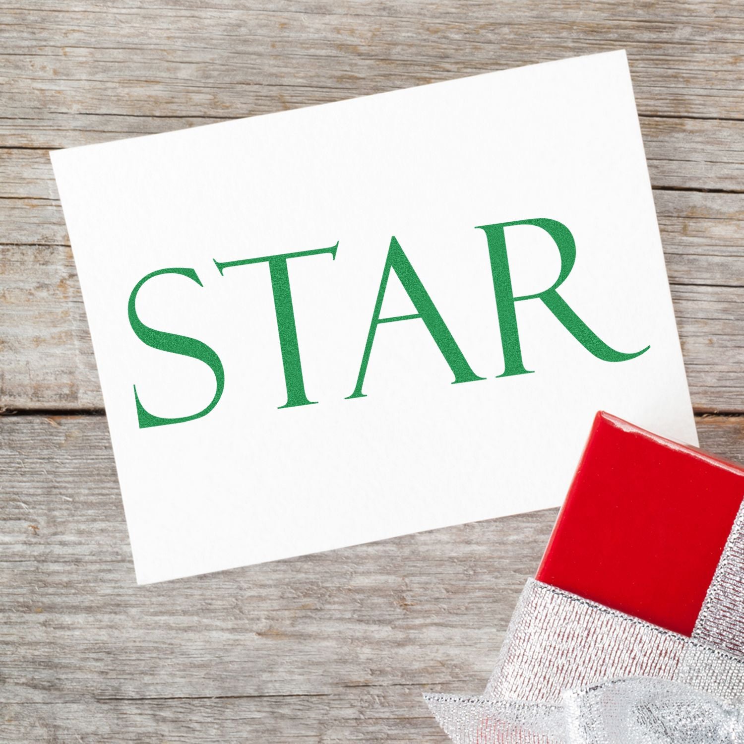 Star Rubber Stamp on white card with green 'STAR' text, placed on wooden surface next to a red gift box with silver ribbon.