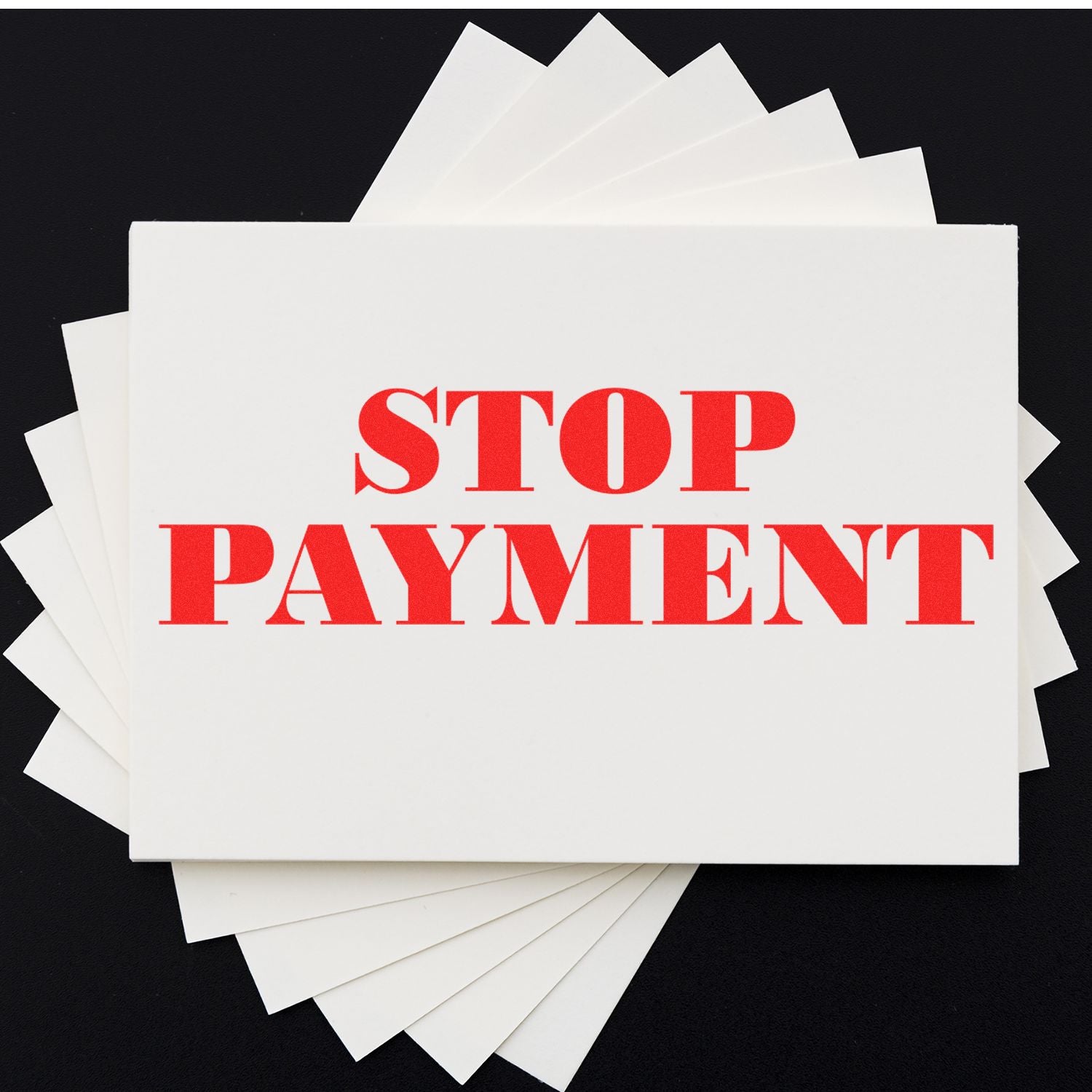 Stop Payment Rubber Stamp in red ink on white paper, with additional blank sheets fanned out underneath on a black background.