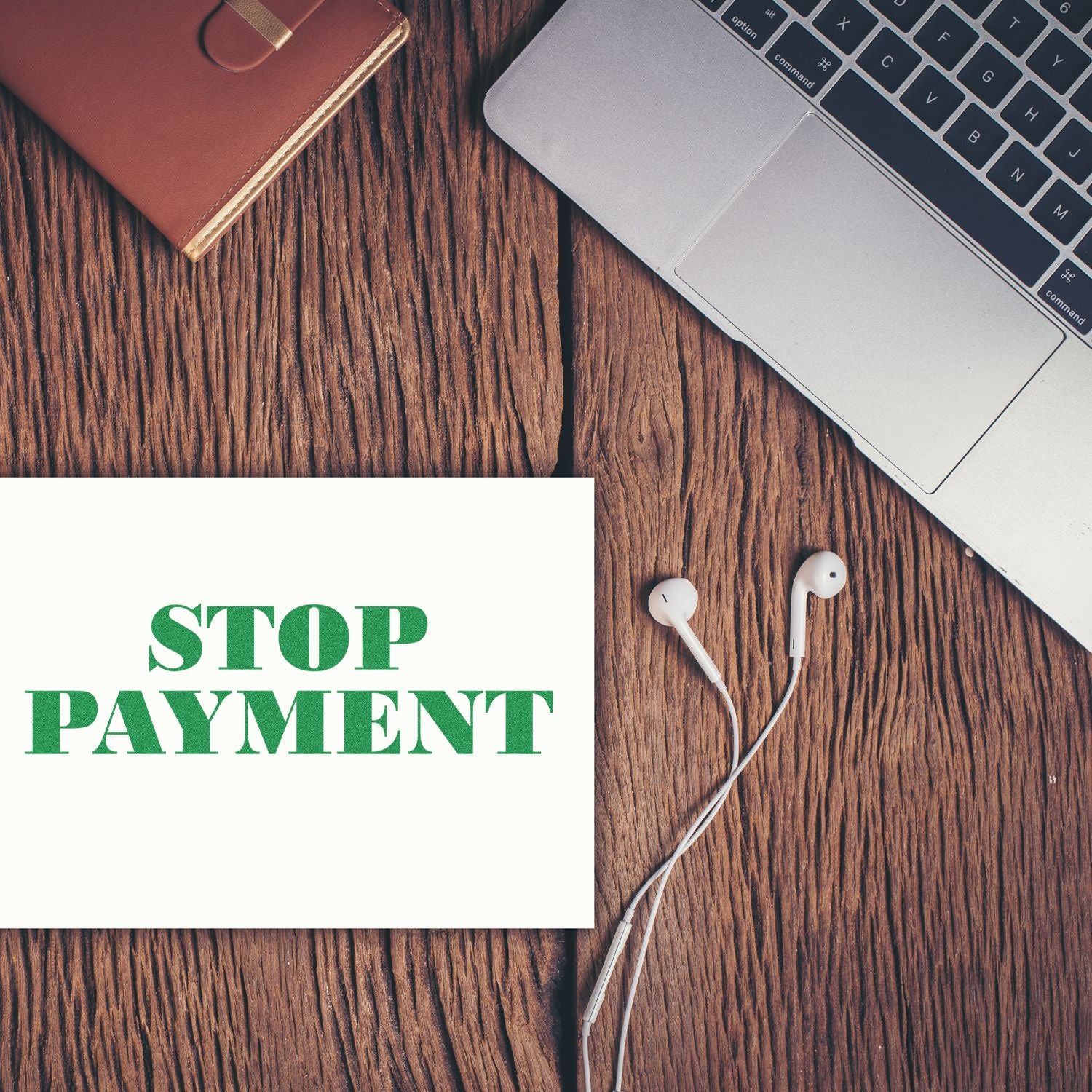 Stop Payment rubber stamp on a white paper next to a laptop, earphones, and a brown notebook on a wooden surface.