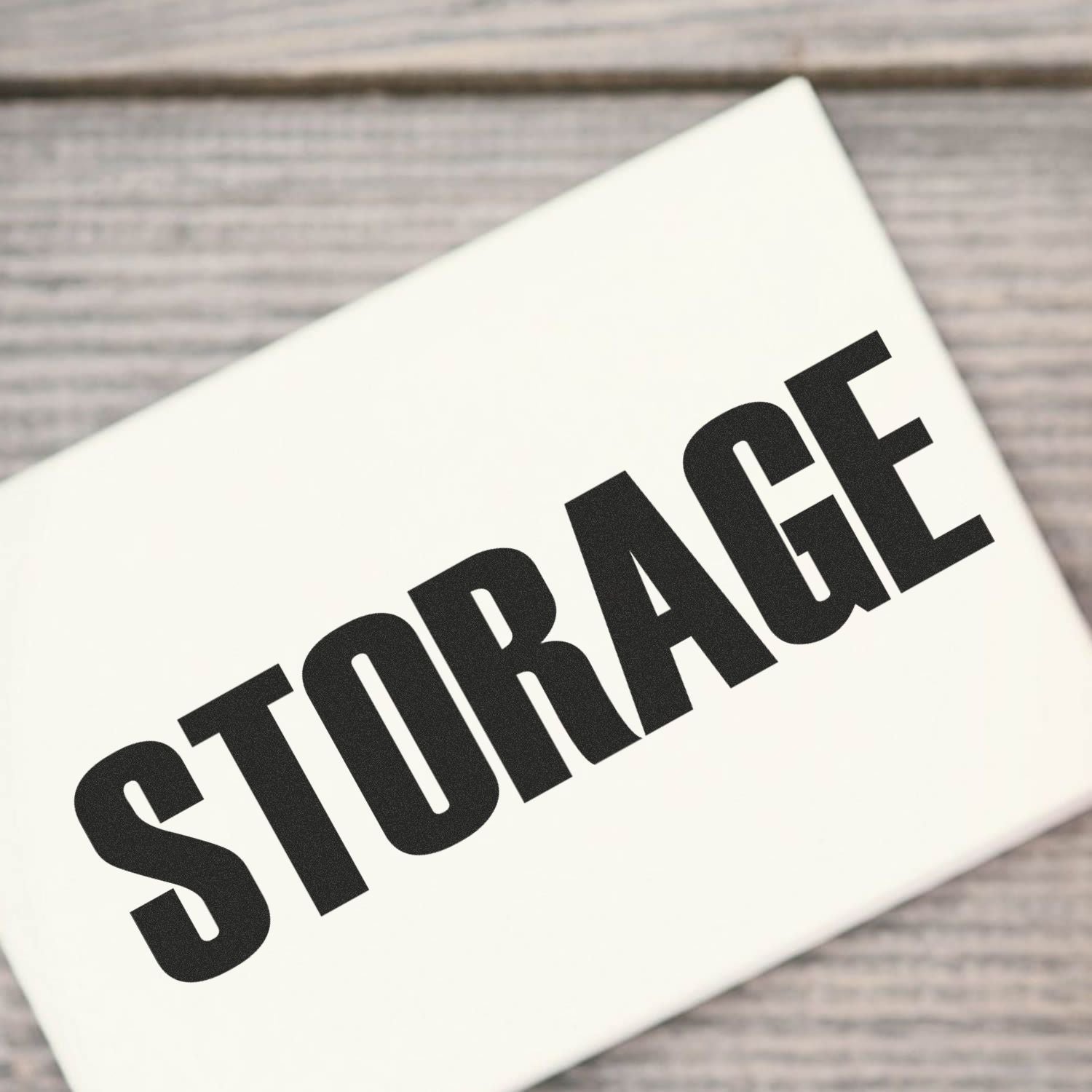 Self Inking Storage Stamp used to label a white box with the word STORAGE in bold black letters, placed on a wooden surface.