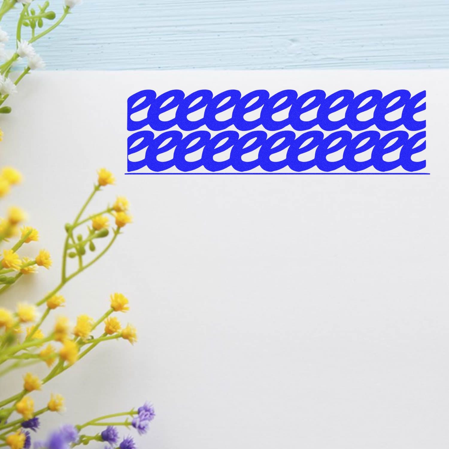 Large Self Inking Strikeout Stamp in use, creating a blue strikeout pattern on white paper, with yellow and purple flowers in the background.