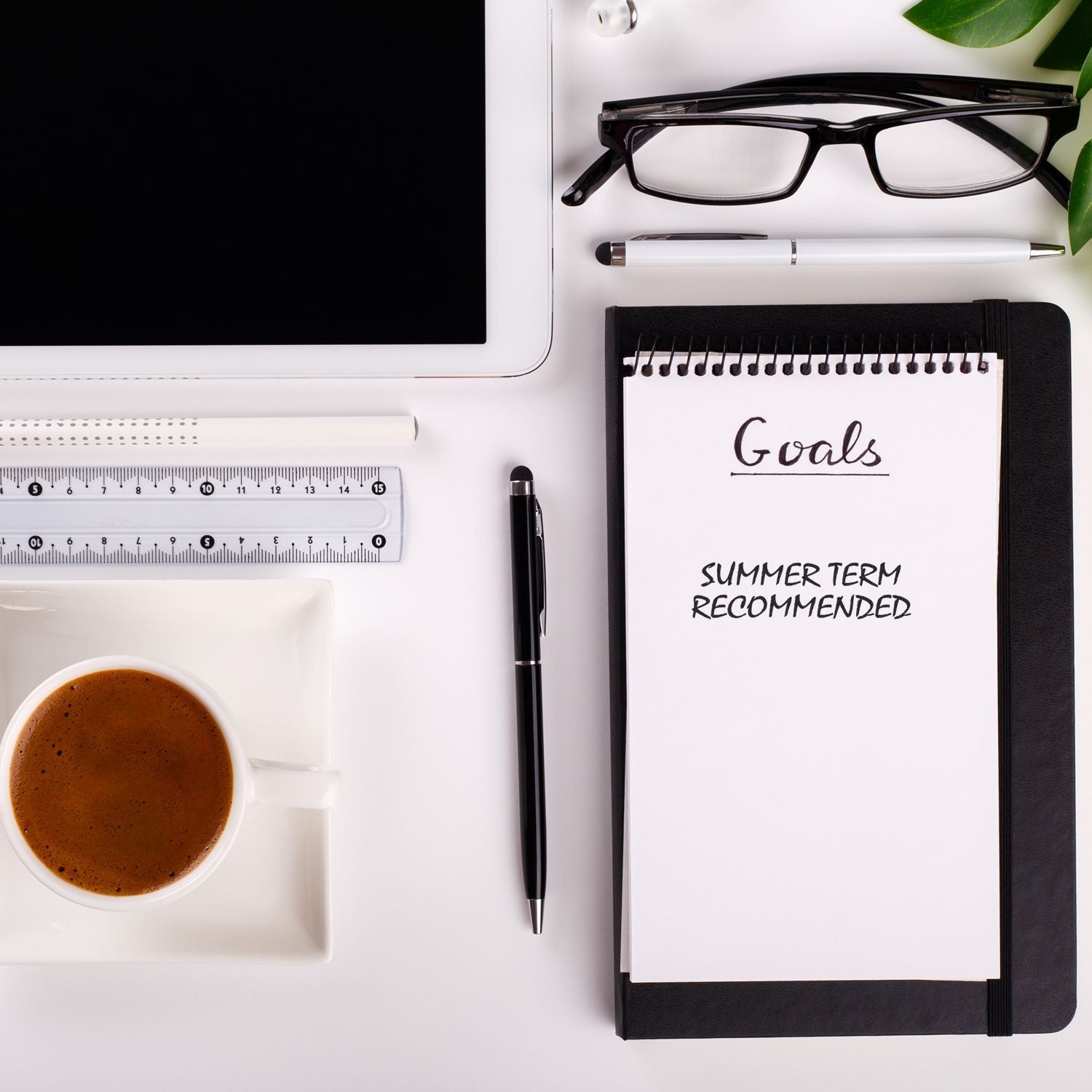 Desk with a Large Self Inking Summer Term Recommended Stamp on a notepad, alongside a coffee cup, tablet, glasses, and stationery items.