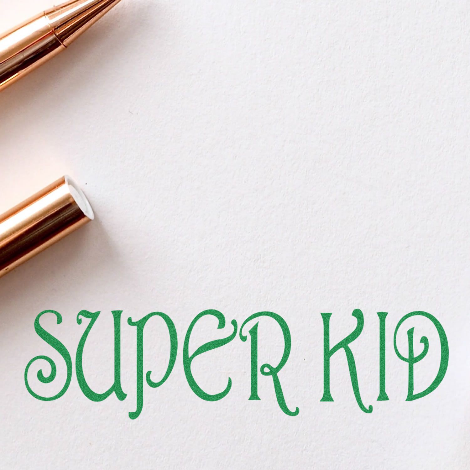 Super Kid Rubber Stamp impression in green ink on white paper with a gold pen beside it.