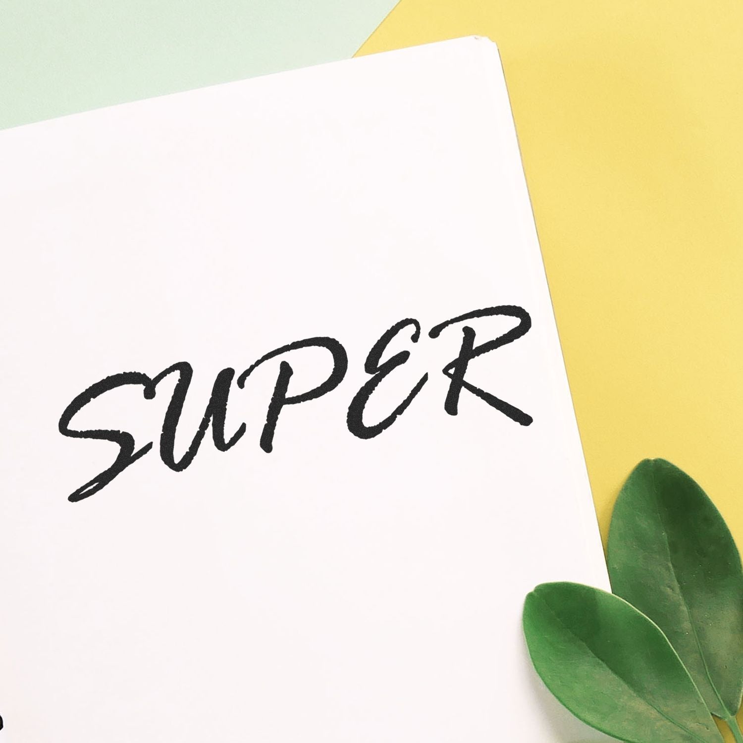 Large Super Rubber Stamp imprinting the word SUPER on white paper, with green leaves and yellow background.