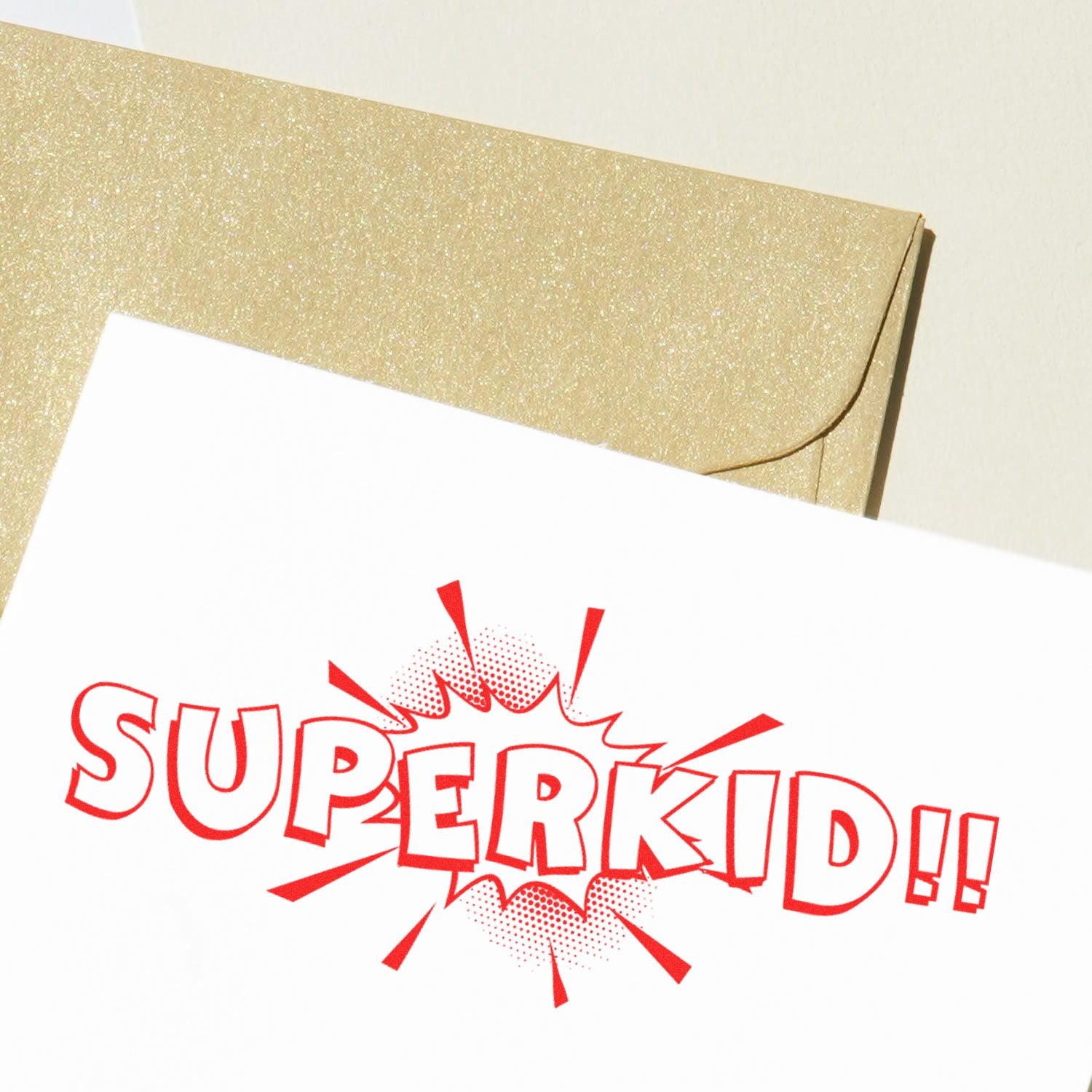 Large Superkid Rubber Stamp imprint in red on white paper, with a gold envelope in the background.