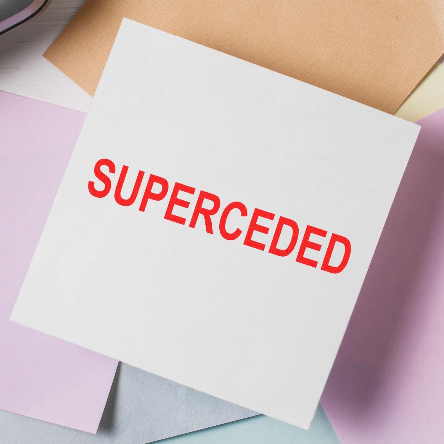 Slim Pre-Inked Superceded Stamp marking SUPERCEDED in red on a white paper, surrounded by pastel-colored papers.