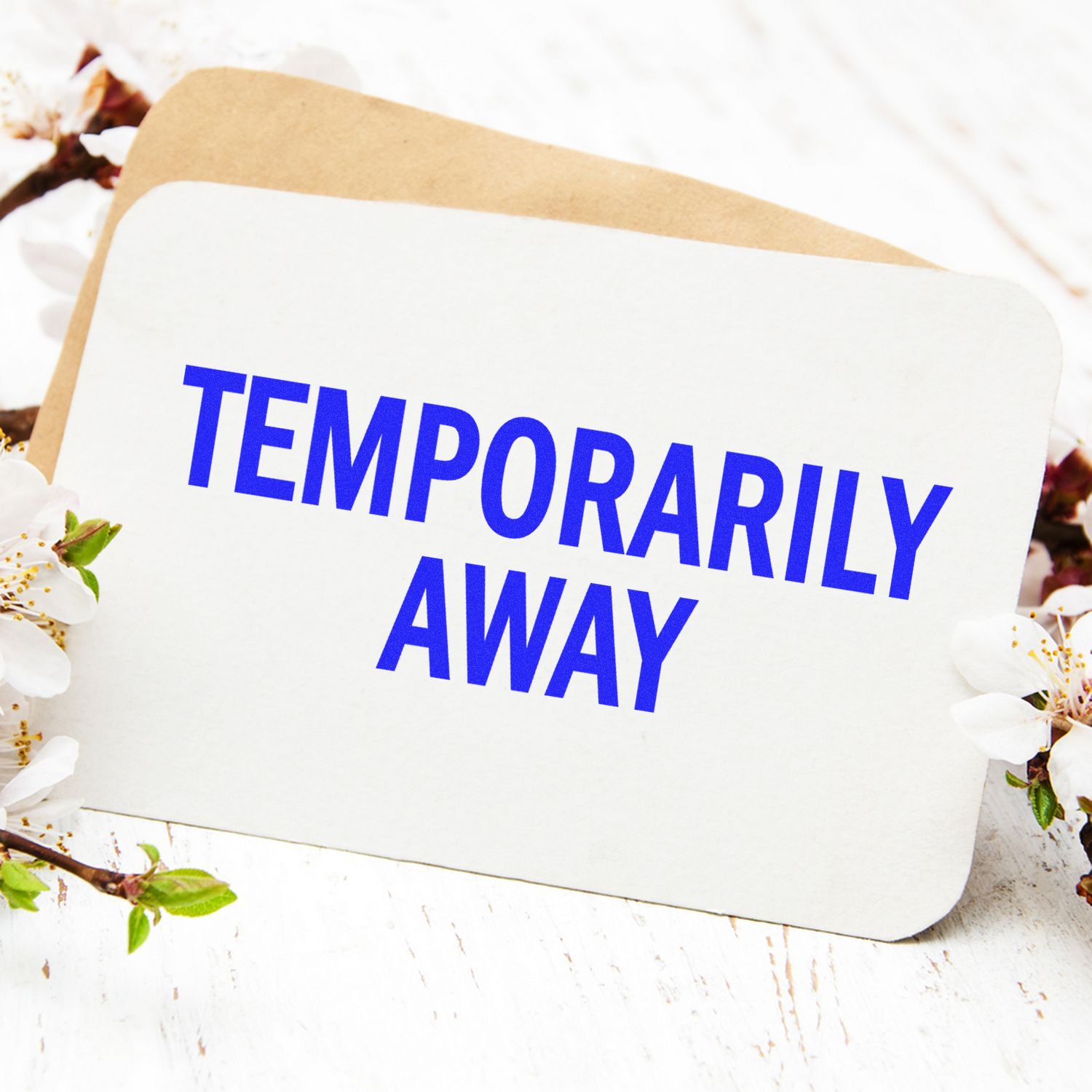 Large Temporarily Away Rubber Stamp on a white card with blue text, surrounded by flowers and a brown envelope in the background.