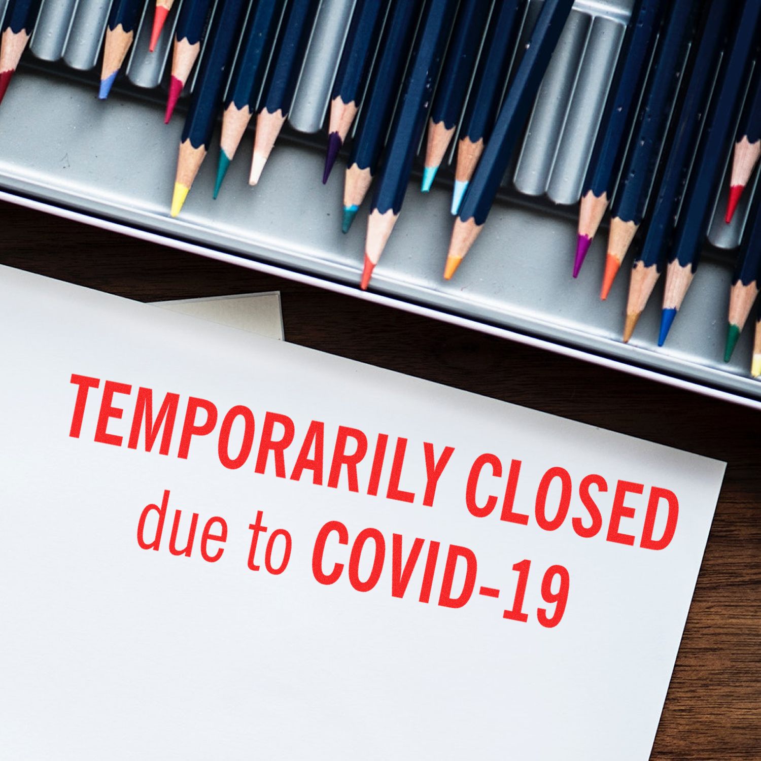 Temporarily Closed rubber stamp on a white paper with colored pencils in the background, indicating closure due to COVID-19.