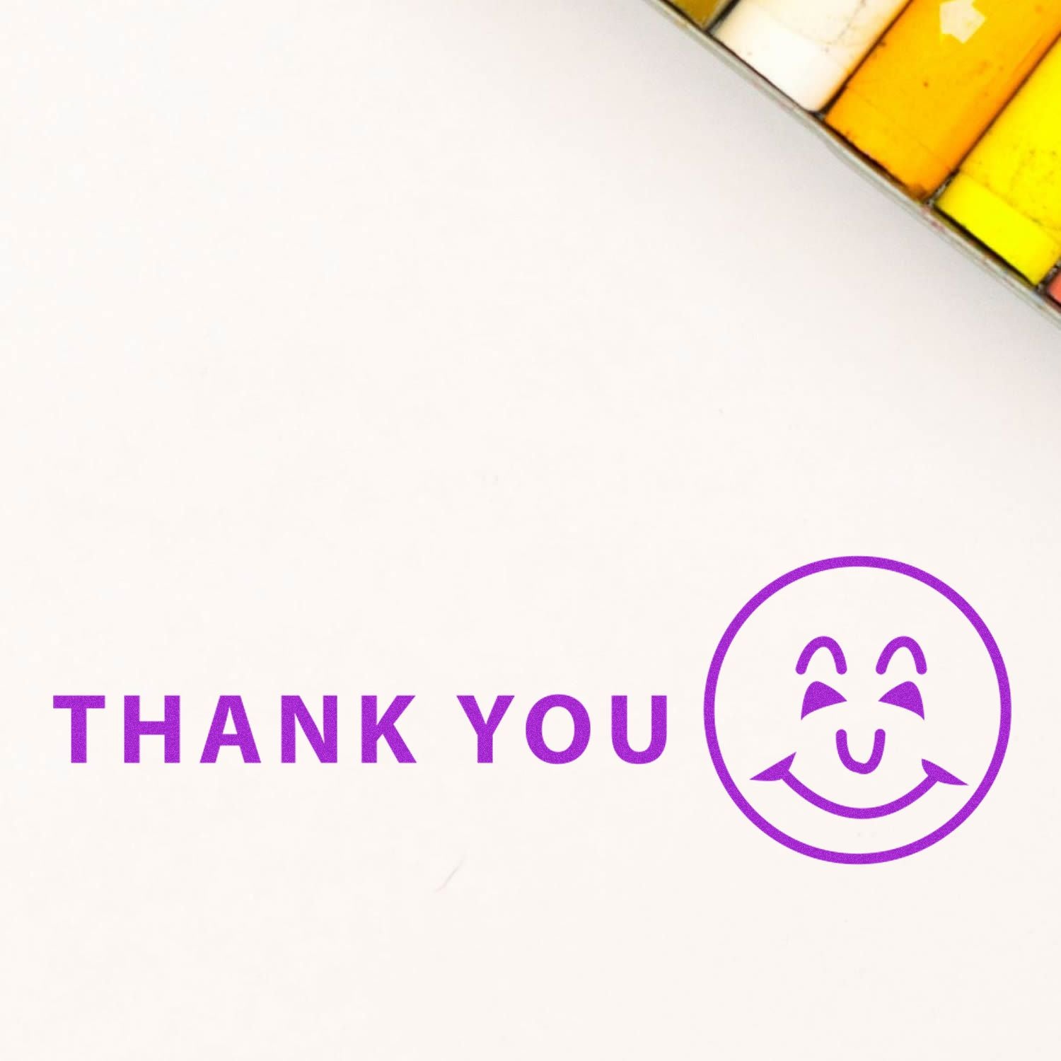 Thank You with Smiley Rubber Stamp in purple ink on white paper, with colored pencils partially visible in the top right corner.