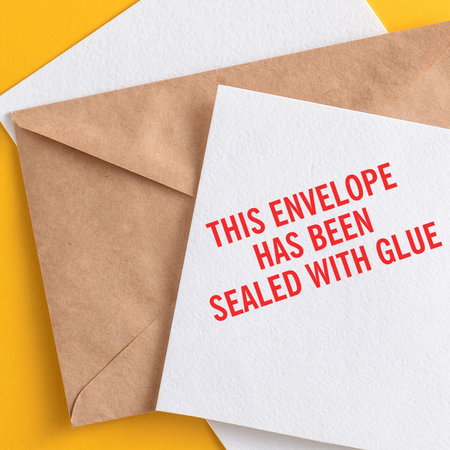 A brown envelope and a white card stamped with This Envelope Has Been Sealed With Glue in red text on a yellow background.