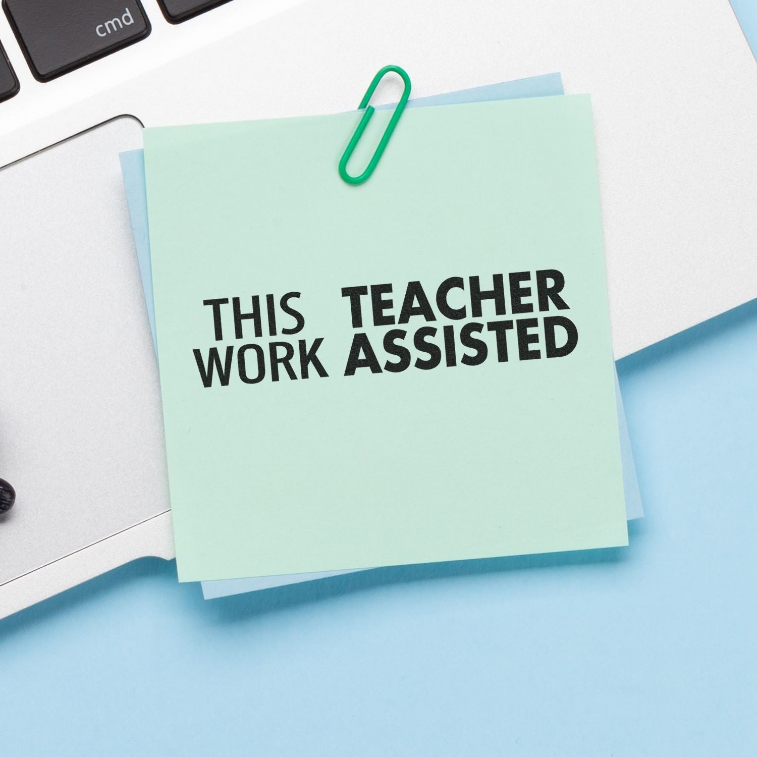 A mint green sticky note with THIS WORK TEACHER ASSISTED stamped on it using the Self Inking This Work Teacher Assisted Stamp, clipped to a laptop.