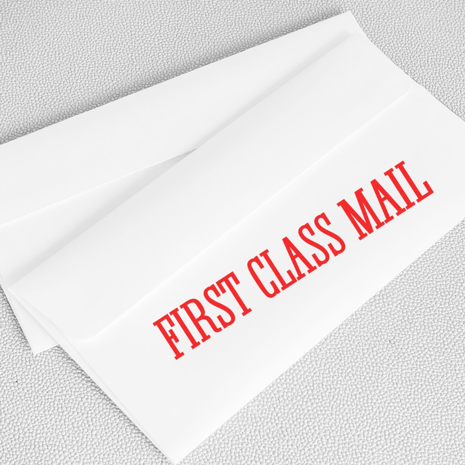 Two white envelopes stamped with FIRST CLASS MAIL in red using a Times First Class Mail Rubber Stamp on a light gray surface.