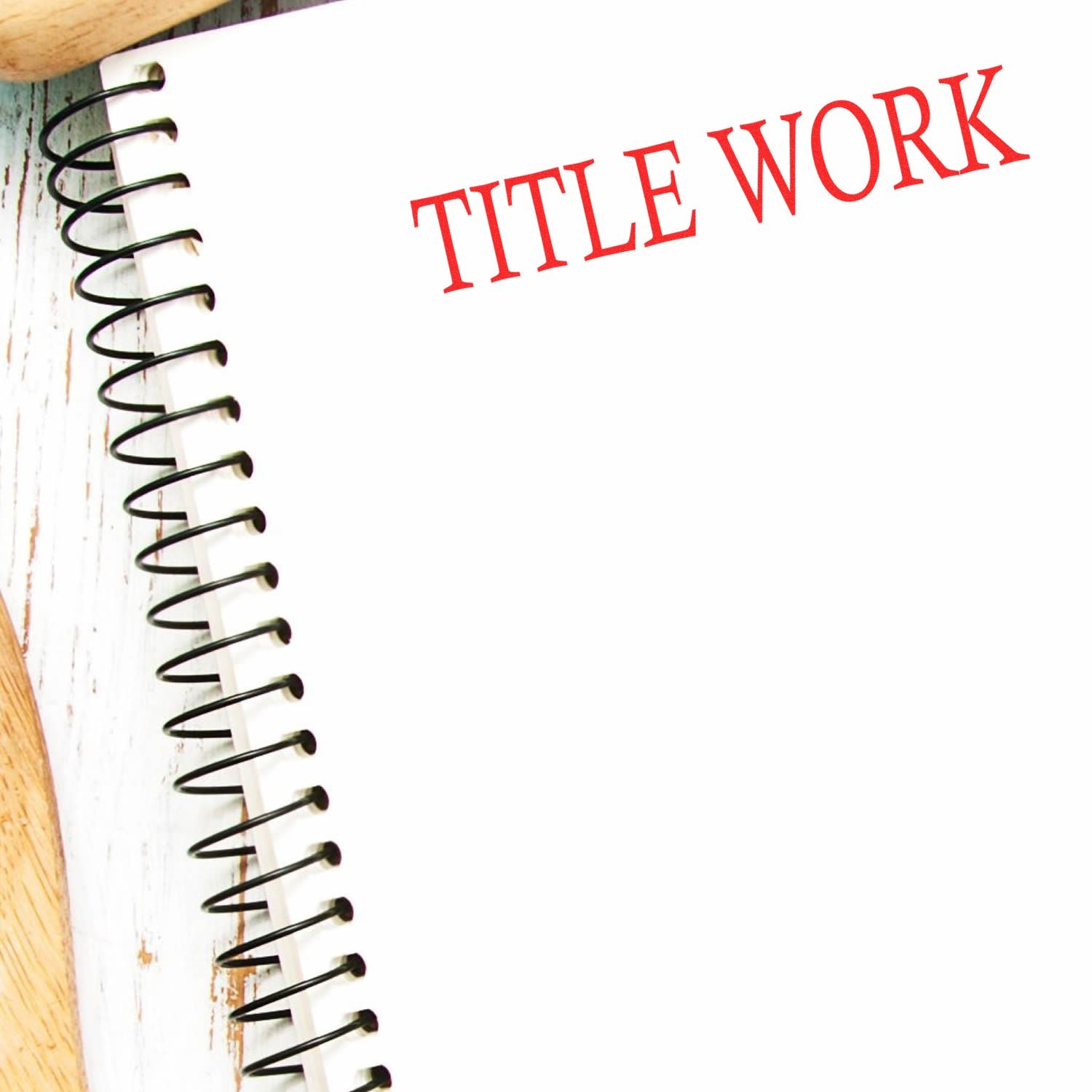 Large Self Inking Title Work Stamp in red ink on a white spiral notebook, placed on a wooden surface.