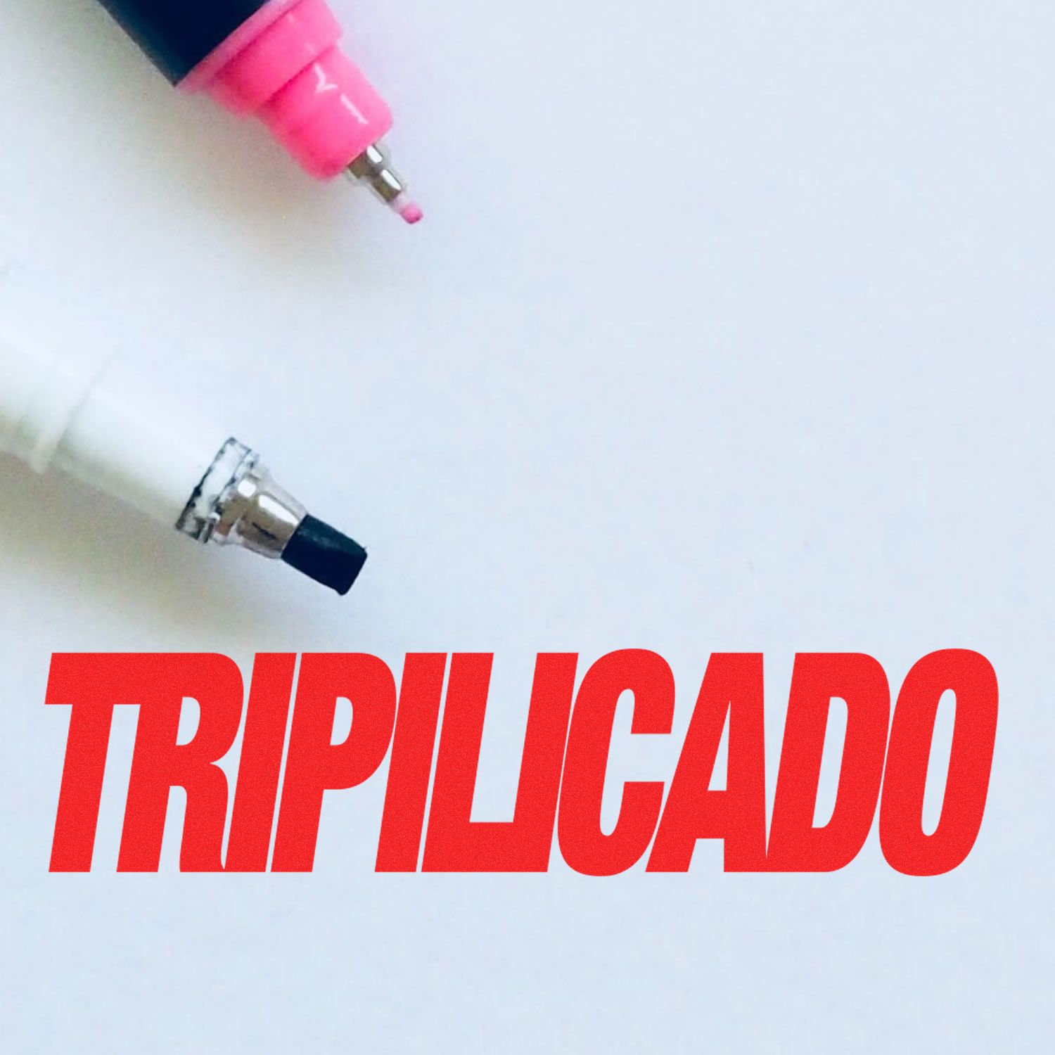 Close-up of a Tripilicado rubber stamp impression in red ink with two marker tips, one pink and one black, on a white background.