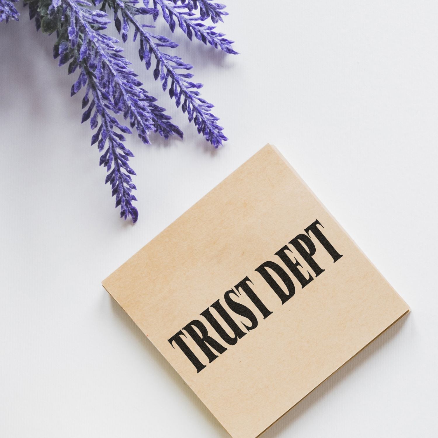 Large Trust Dept rubber stamp on a beige square block, placed on a white surface next to purple lavender flowers.