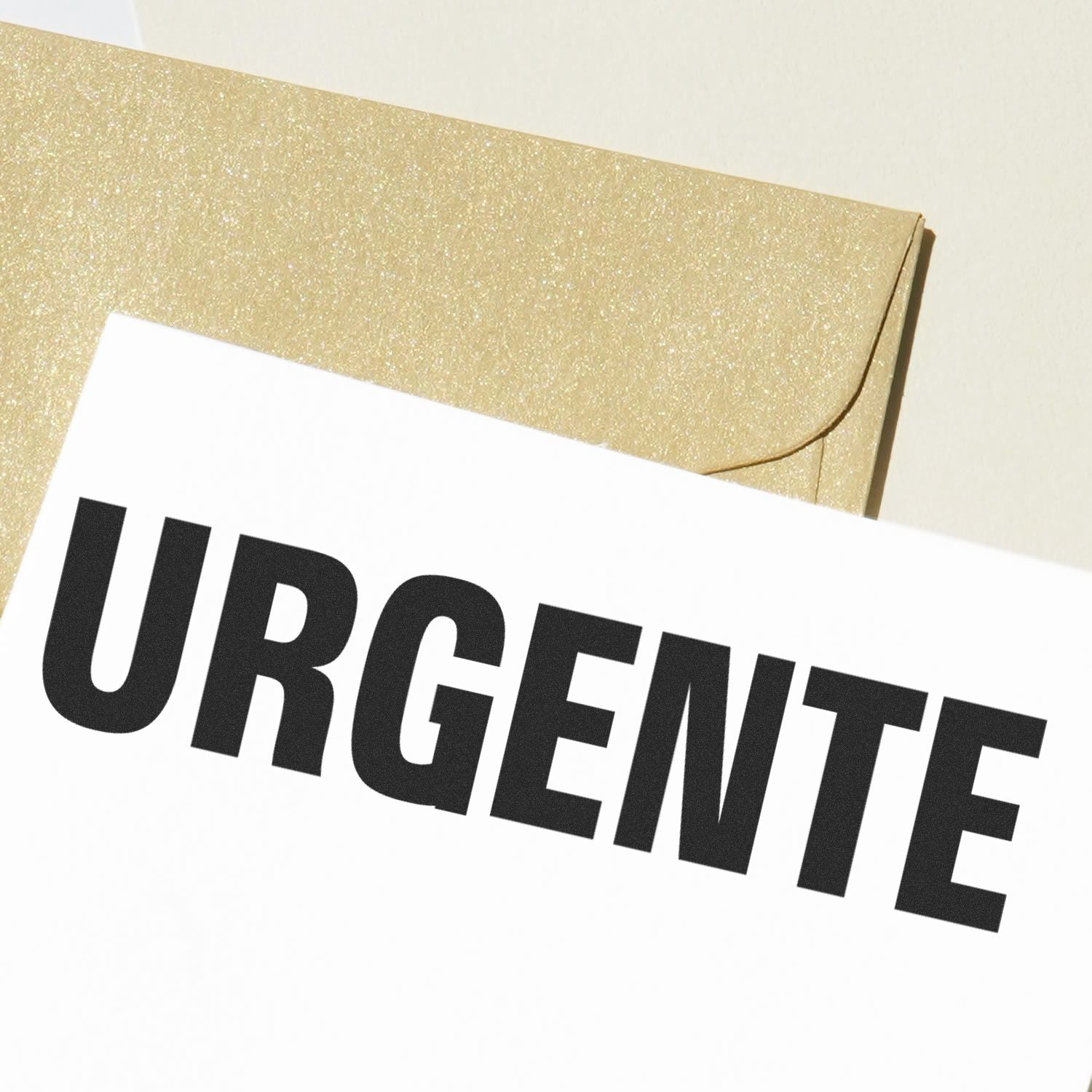 Large Urgente Rubber Stamp in black ink on a white paper, with a gold envelope in the background.