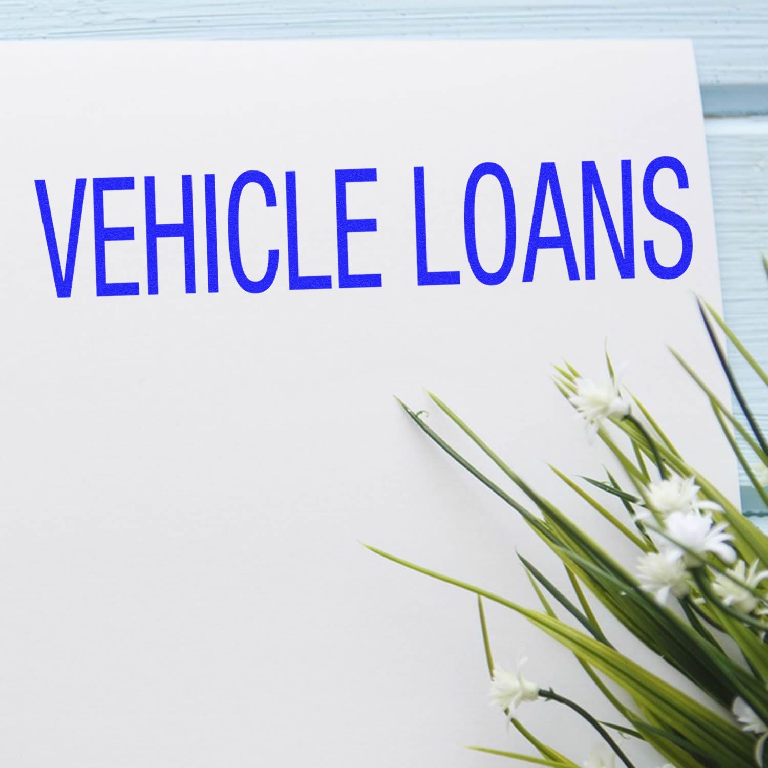 Large Pre-Inked Vehicle Loans Stamp in blue ink on white paper, with green and white flowers in the foreground.